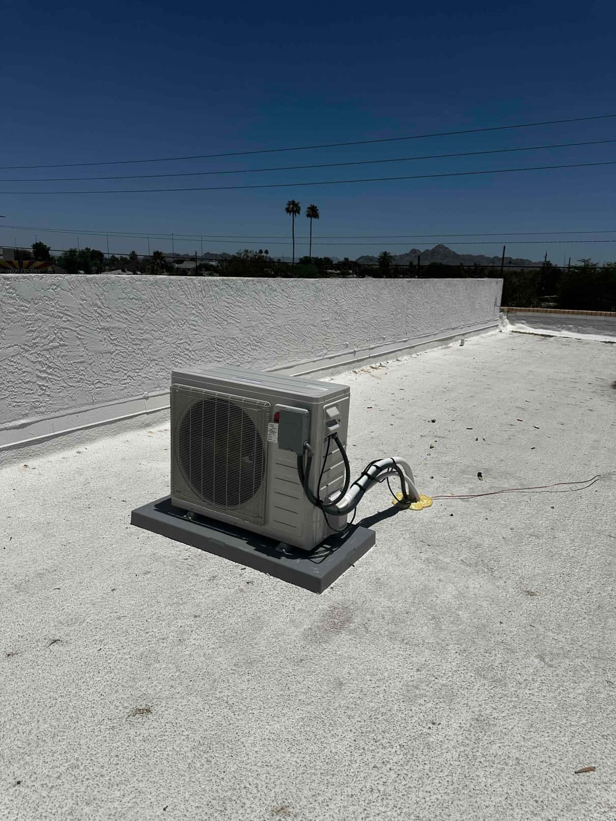 Mini-split condenser set on a rooftop pad with insulated line set and sealed wall penetration along the parapet.