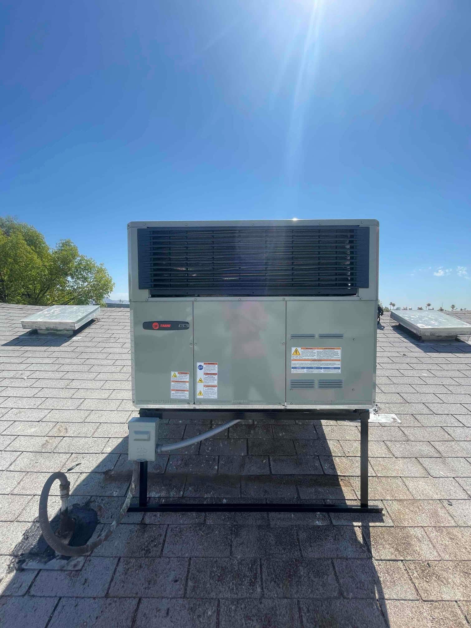 New rooftop packaged unit installed on a metal stand with sealed electrical whip and rooftop disconnect box.