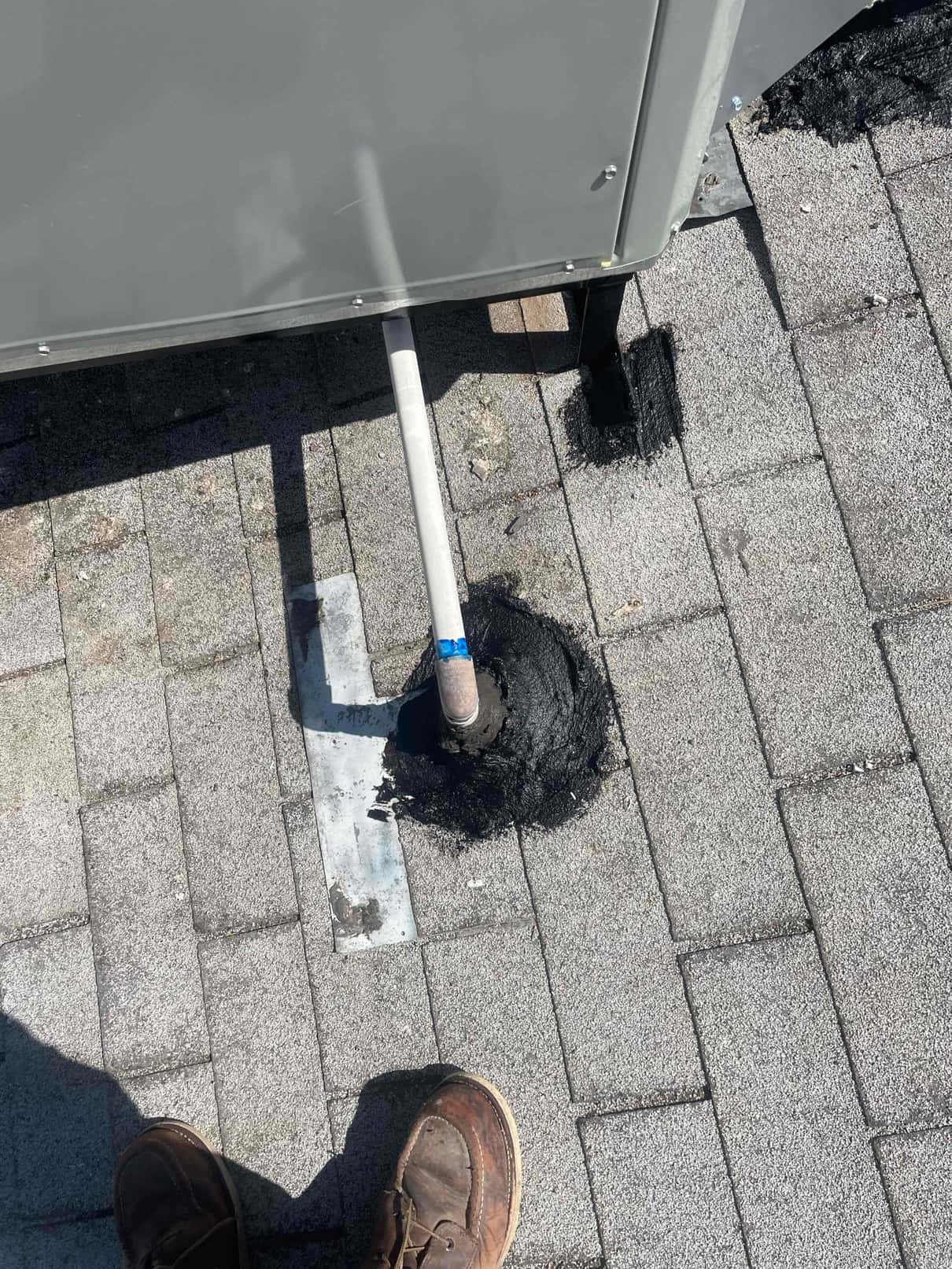 Roof penetration sealed around a condensate drain or line set near the packaged HVAC unit base with flashing and mastic.