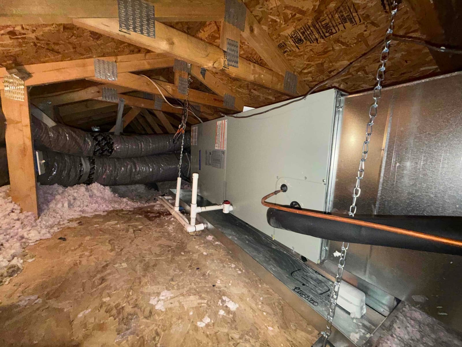 Air handler installed in attic with insulated flex ducts, new condensate drain piping, and copper refrigerant lines on a secondary drain pan.