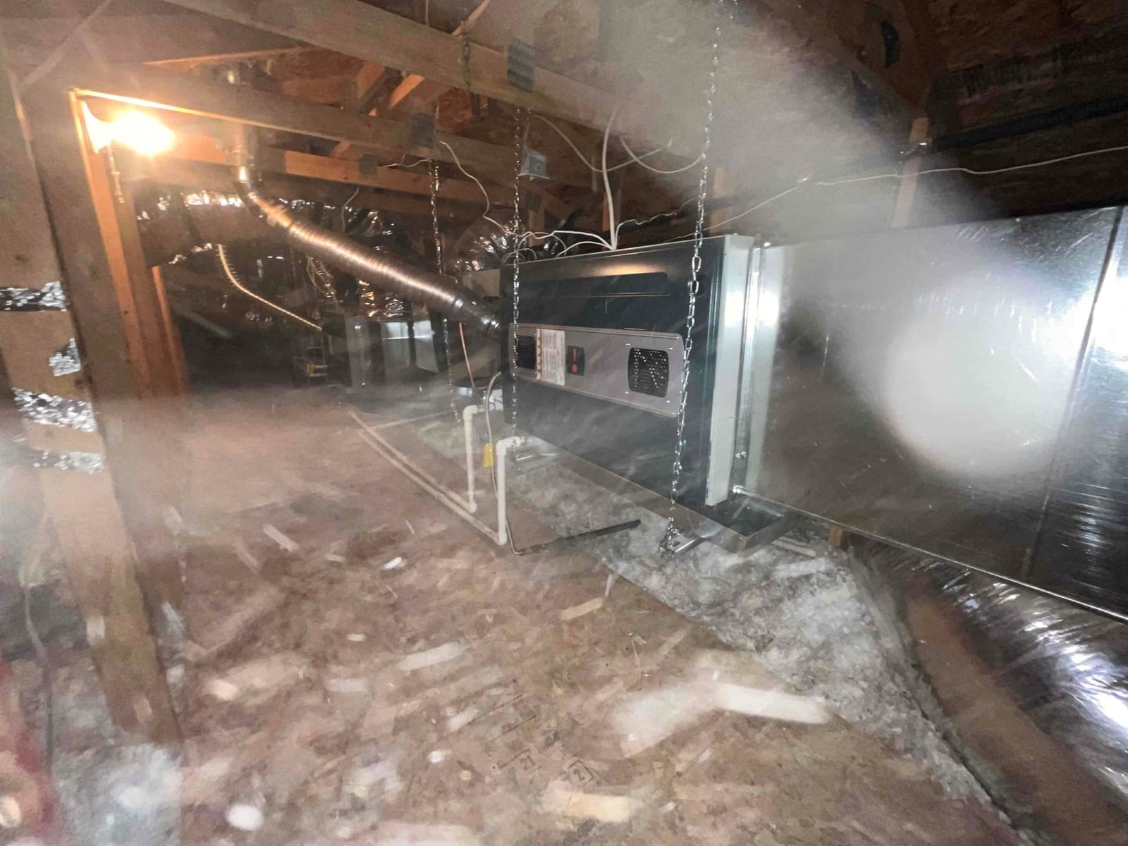 Air handler suspended from ceiling chains in attic with new duct connections, drain line, and metal plenum installed.