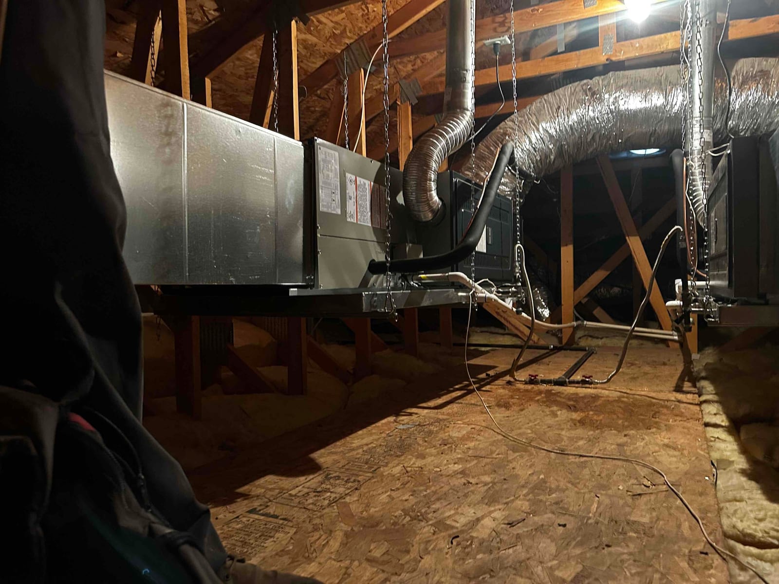 Two air handlers suspended in an attic with insulated flex duct connections, condensate drains, and refrigerant lines routed and supported.