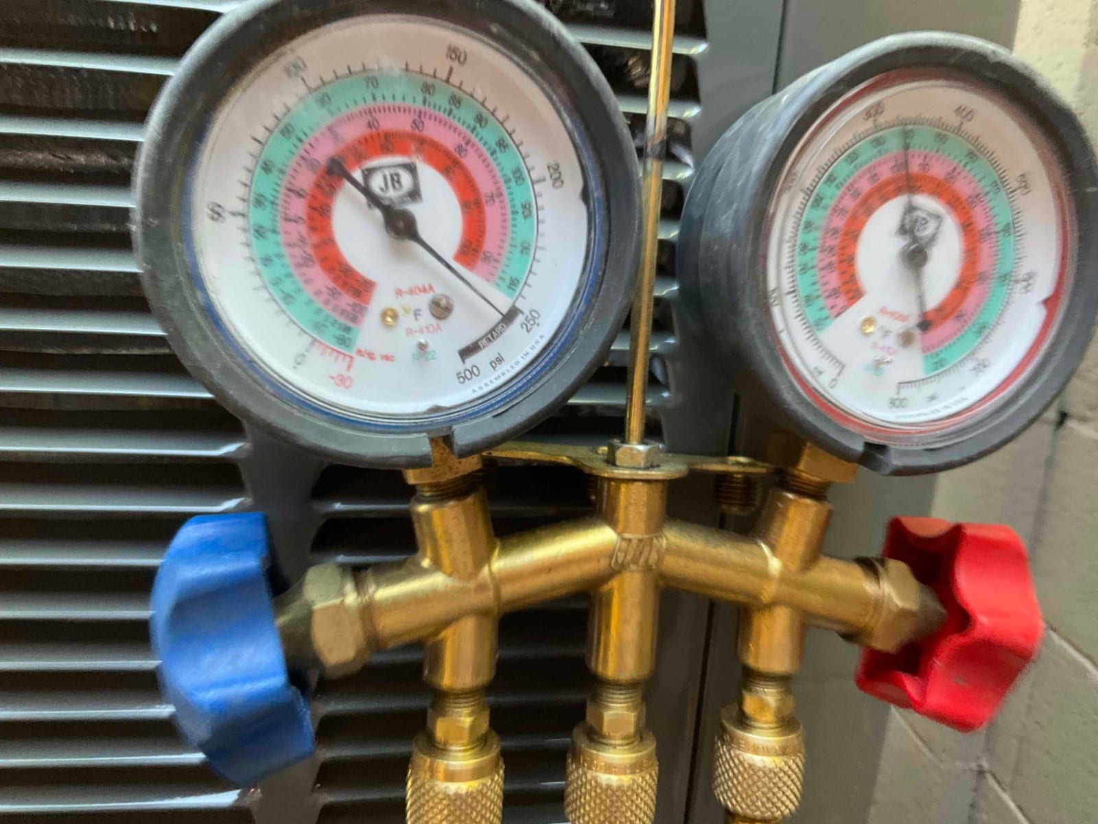 Analog manifold gauges show equal high pressure on both sides during a nitrogen pressure test at the outdoor condenser.