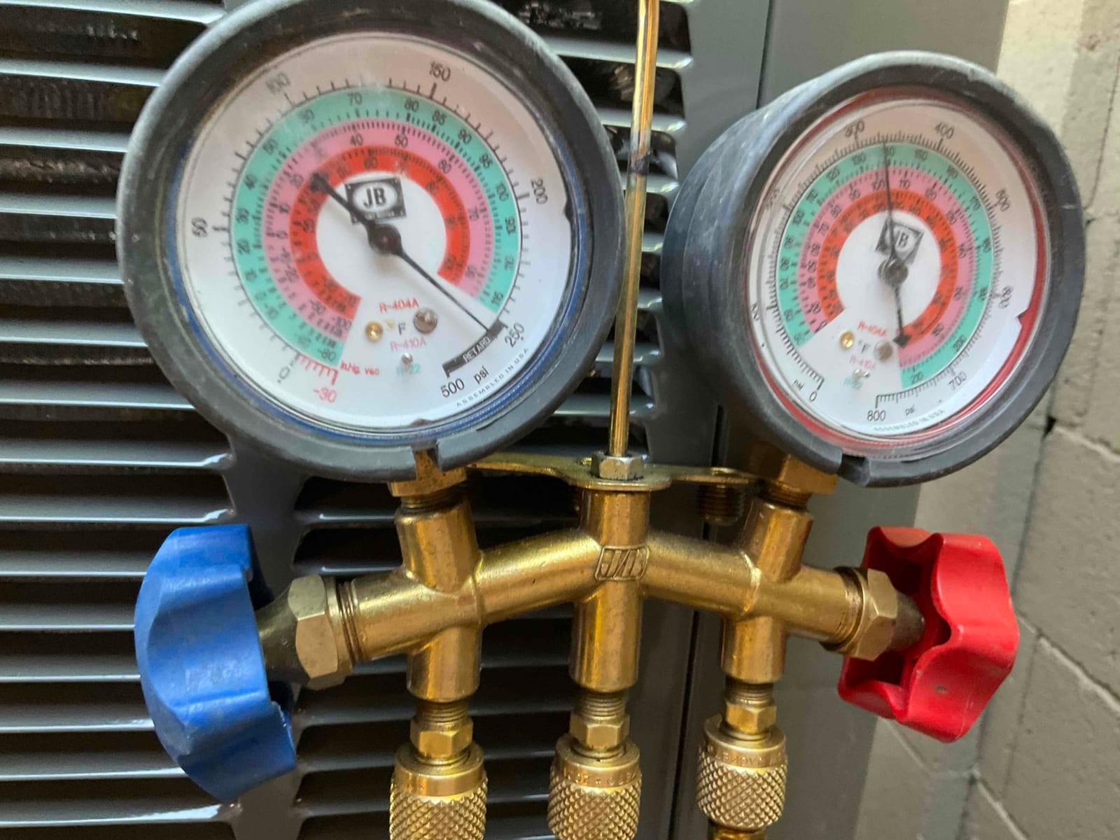 Analog manifold gauges show equal pressure on both sides during a nitrogen pressure test at the outdoor condenser.