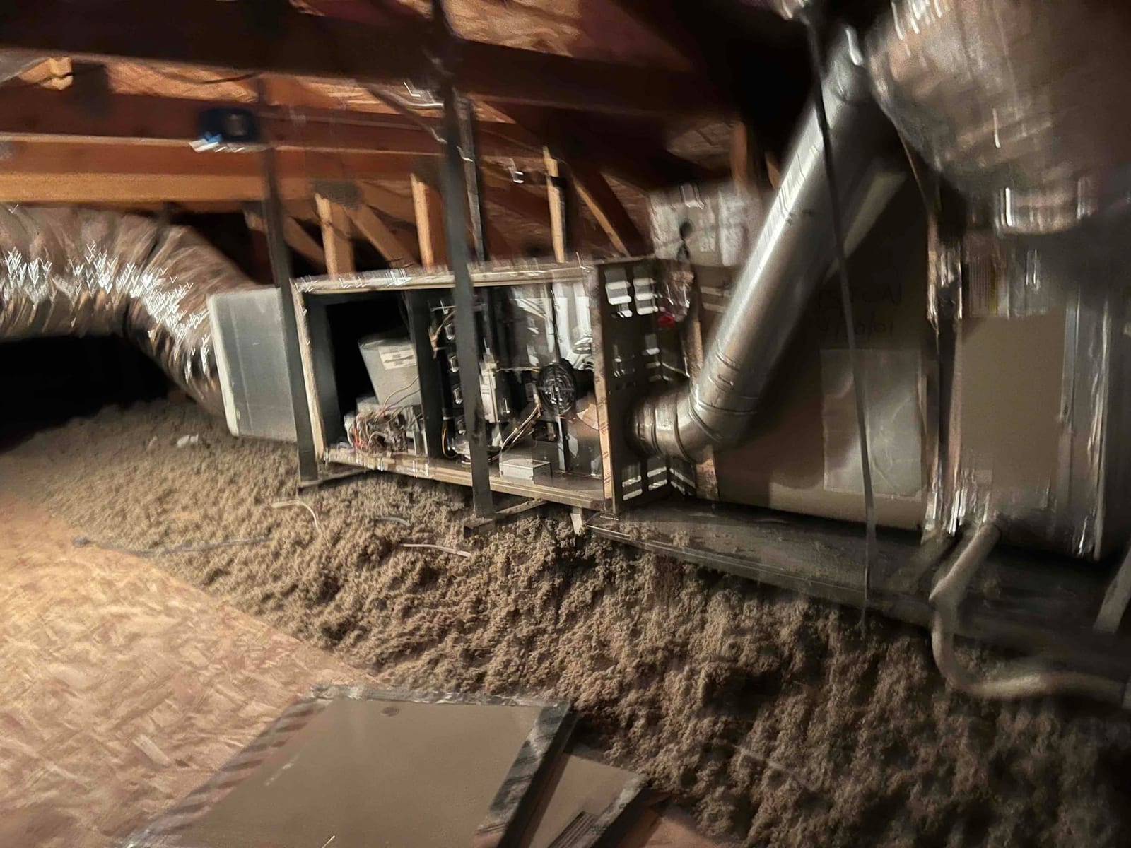 Attic equipment cabinet with access panel removed, exposing wiring and components, connected to flexible duct and metal vent.