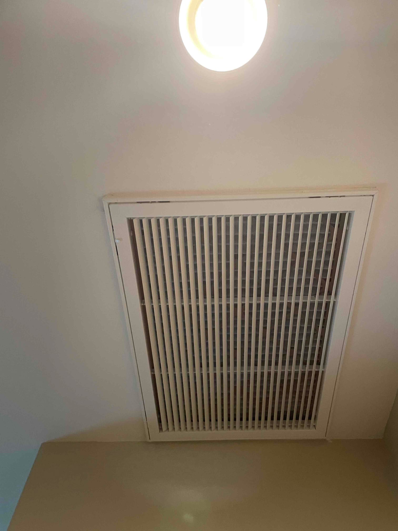 Ceiling-mounted return air grille installed flush with drywall near a recessed light, showing clean louvers and secure fasteners.