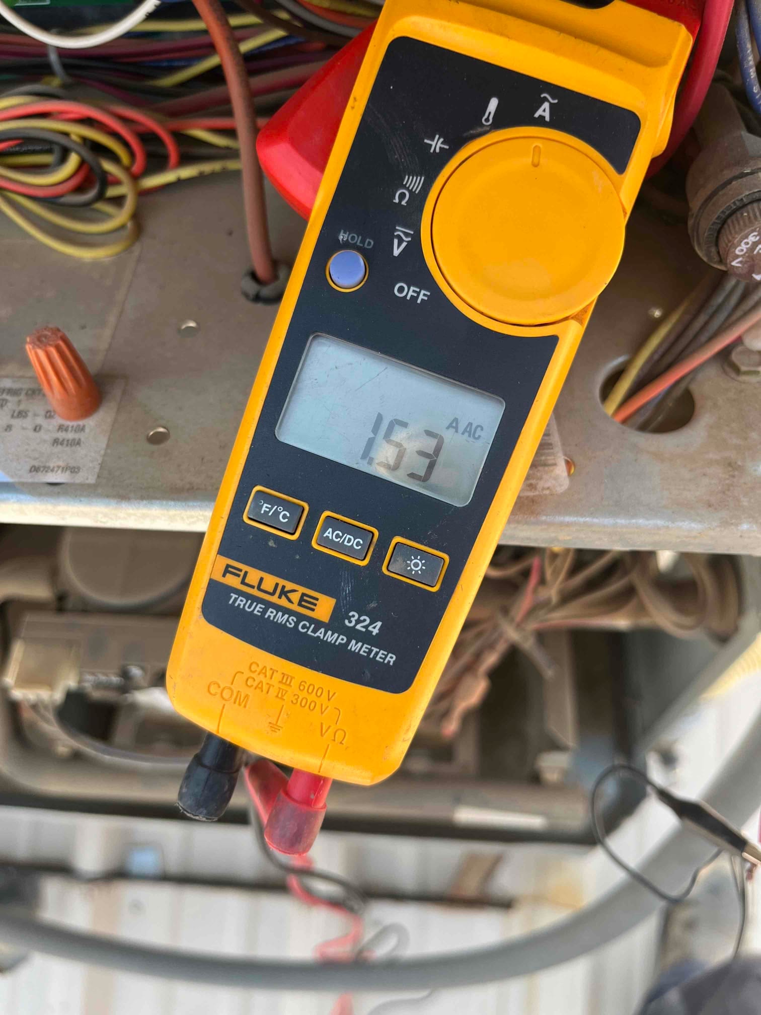 Clamp meter displays 15.3 A AC current while measuring an HVAC circuit conductor at the outdoor unit.