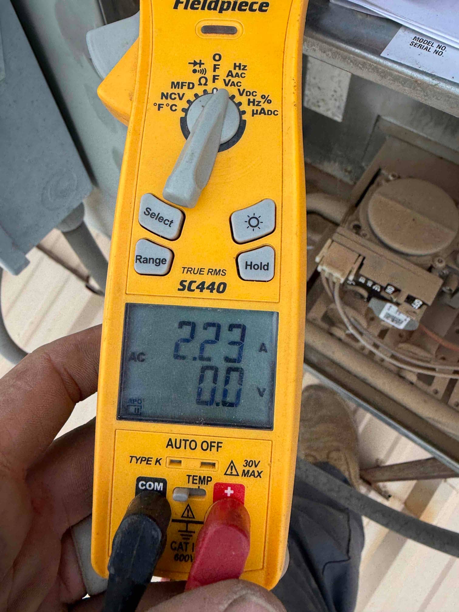 Clamp meter displays 2.23 A AC current on a conductor inside the outdoor condenser electrical compartment.