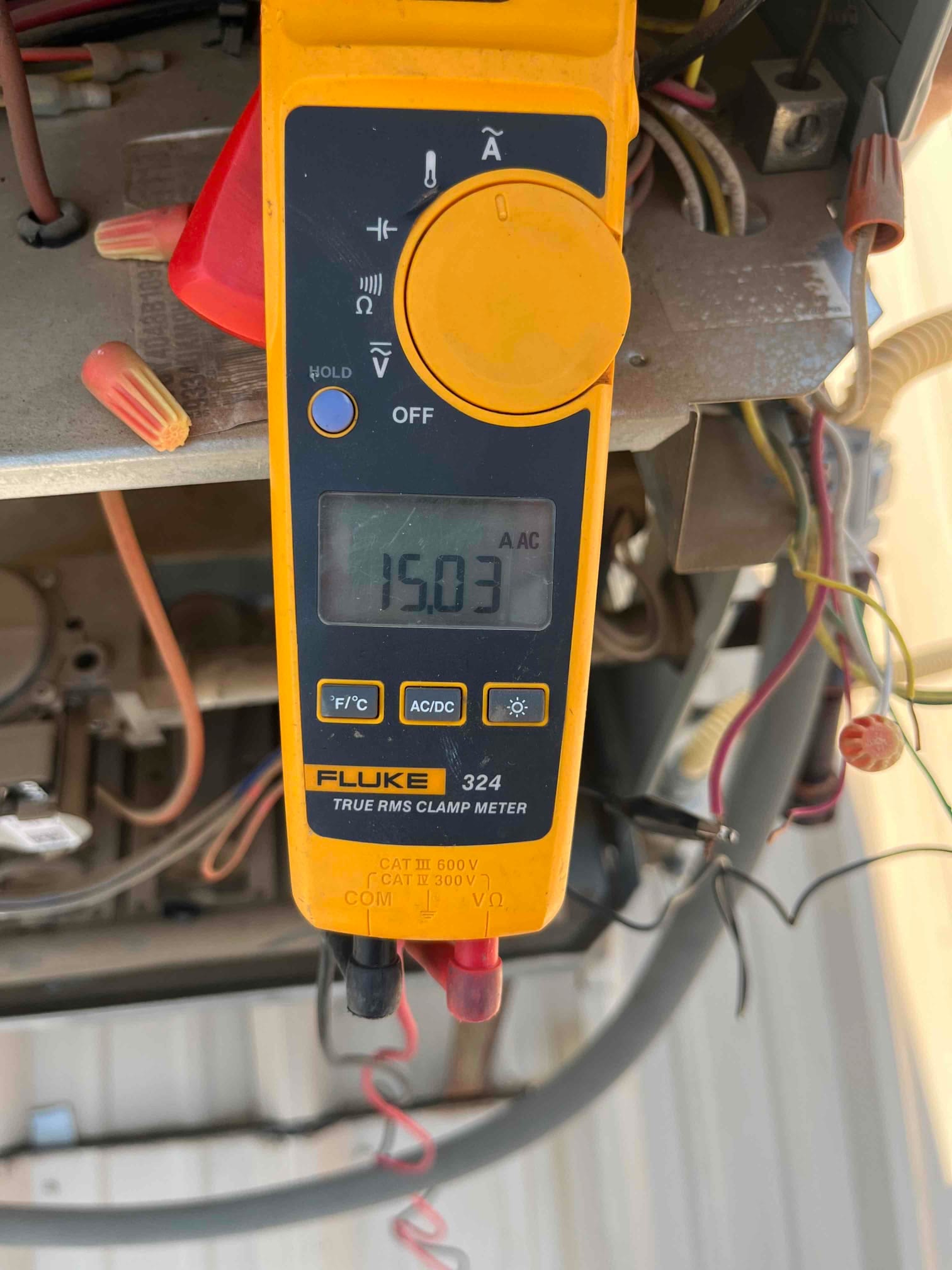 Clamp meter shows 15.03 A AC on a conductor inside the outdoor condenser control compartment during operation.