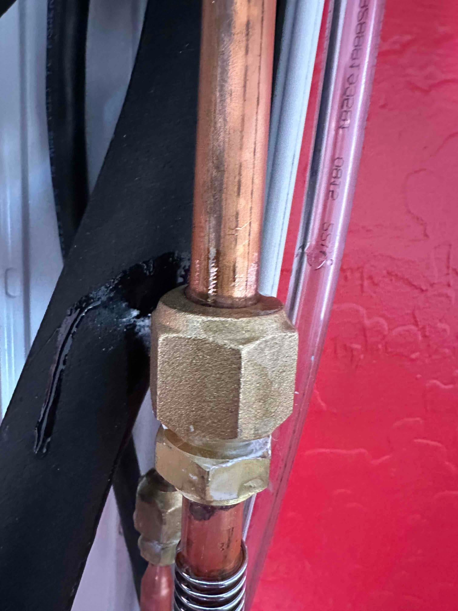 Close-up of mini-split line set connections with flare nuts and insulated suction line at the indoor unit penetration.
