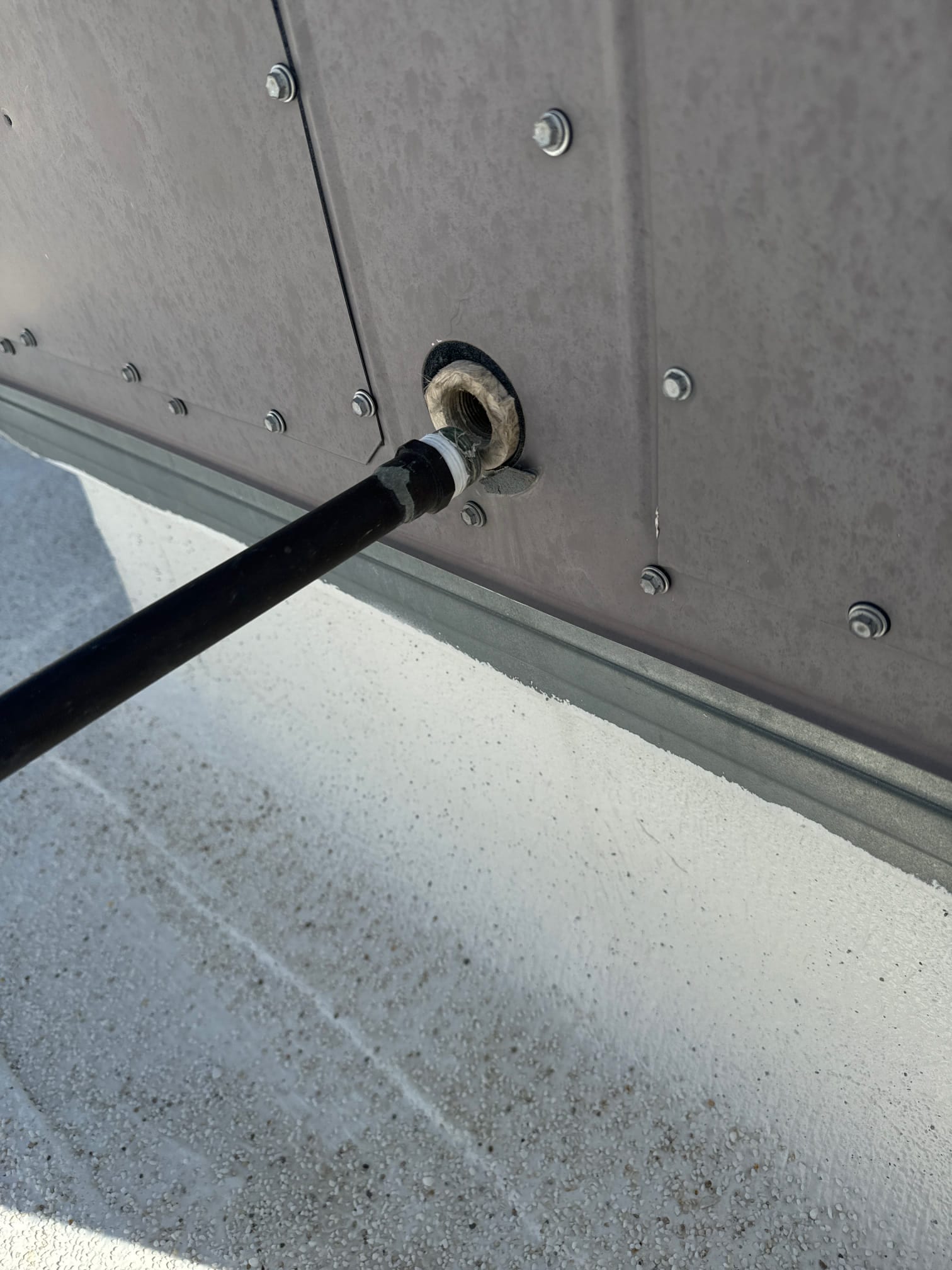 Condensate drain line penetrates the unit cabinet, showing sealed grommet and exterior connection at the rooftop curb.