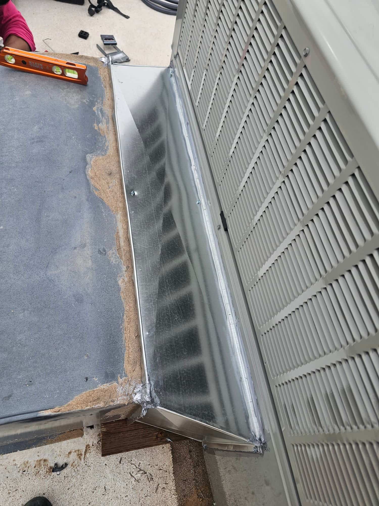 Custom sheet-metal curb adapter sealed and fastened to the rooftop unit base, with a level on the adjacent platform.