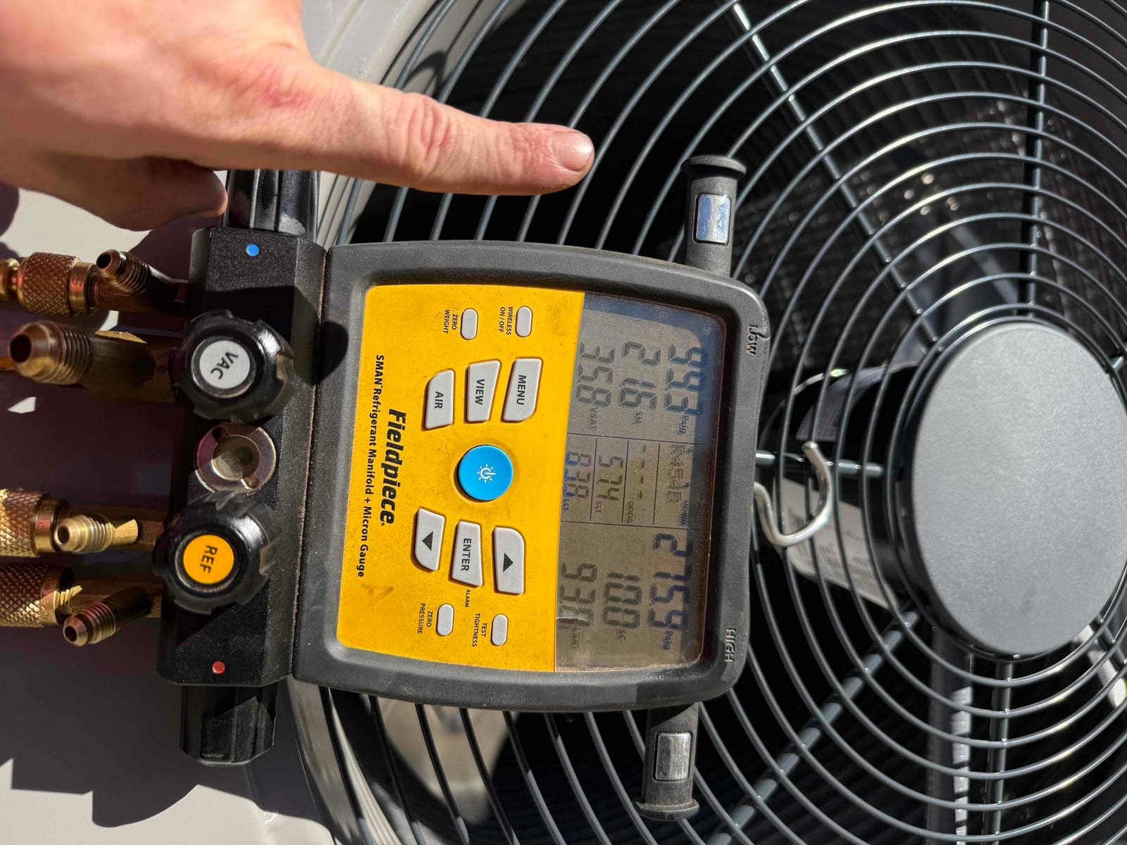 Digital manifold attached at the outdoor unit shows operating suction and liquid pressures while the condenser runs during commissioning.
