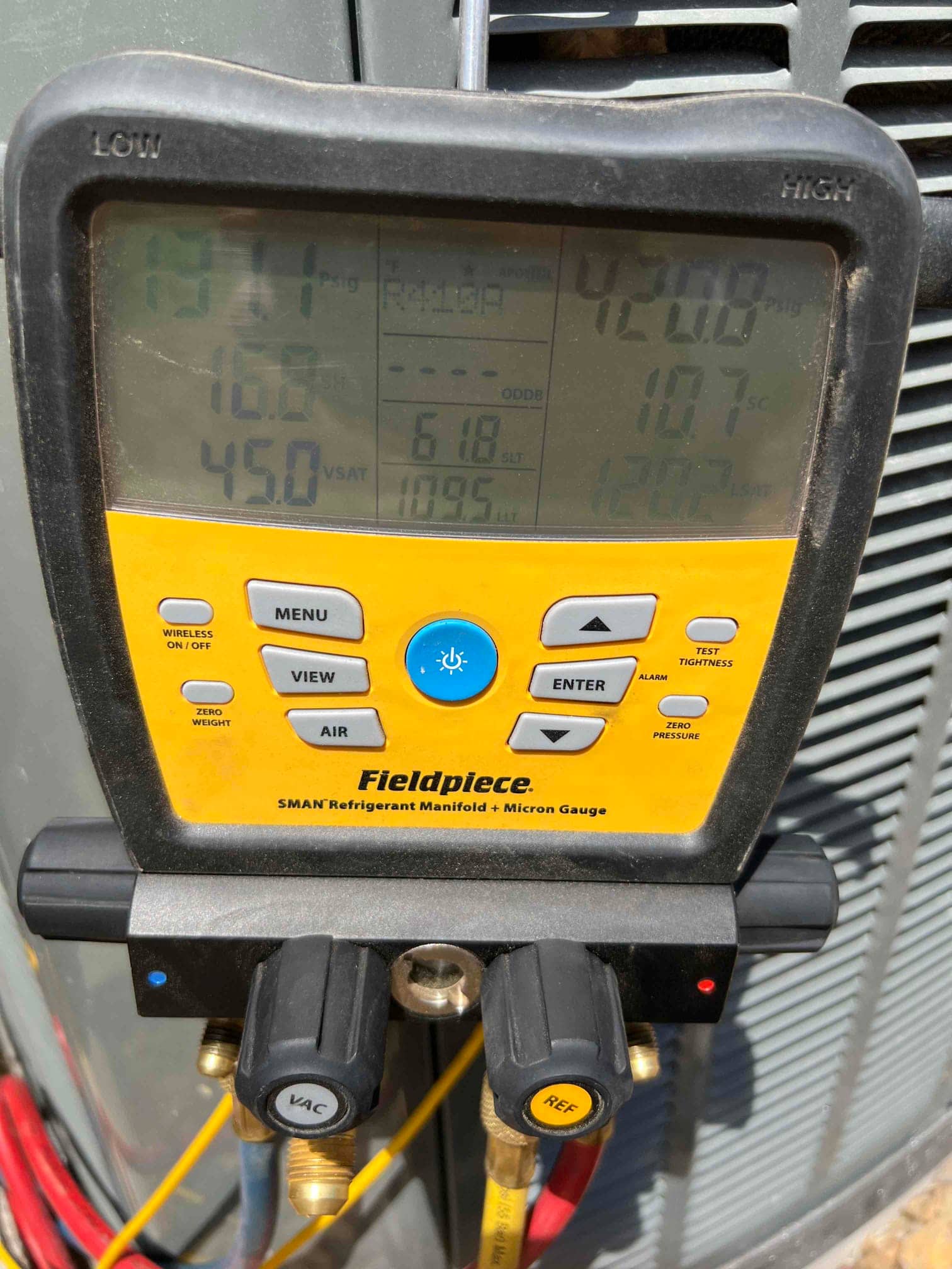 Digital manifold connected to the outdoor unit shows operating refrigerant pressures during system commissioning.
