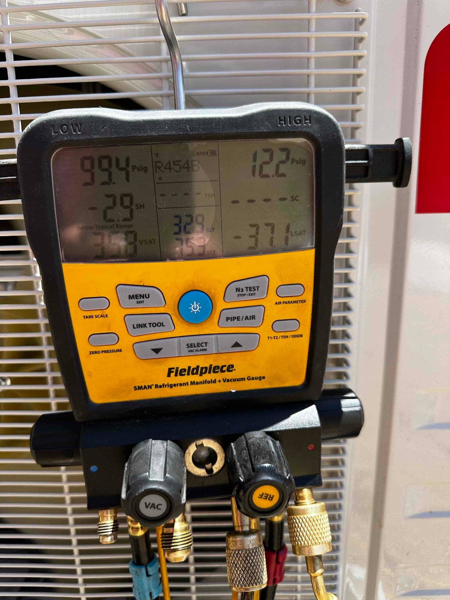 Digital manifold connected to the system shows operating pressures and refrigerant type during commissioning at the outdoor unit.