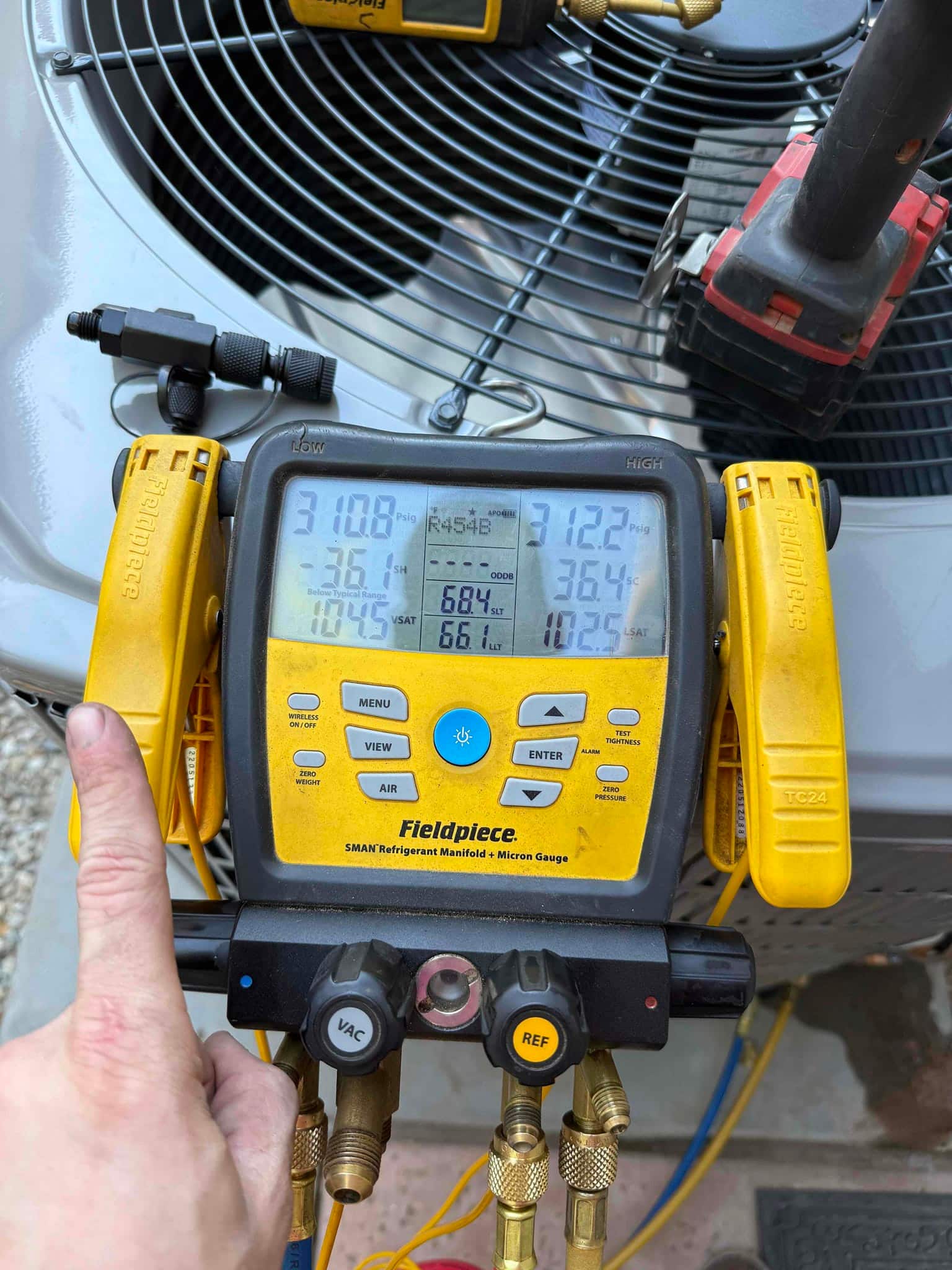 Digital manifold gauges show operating pressures on an outdoor condenser during commissioning, with R-454B selected on the display.