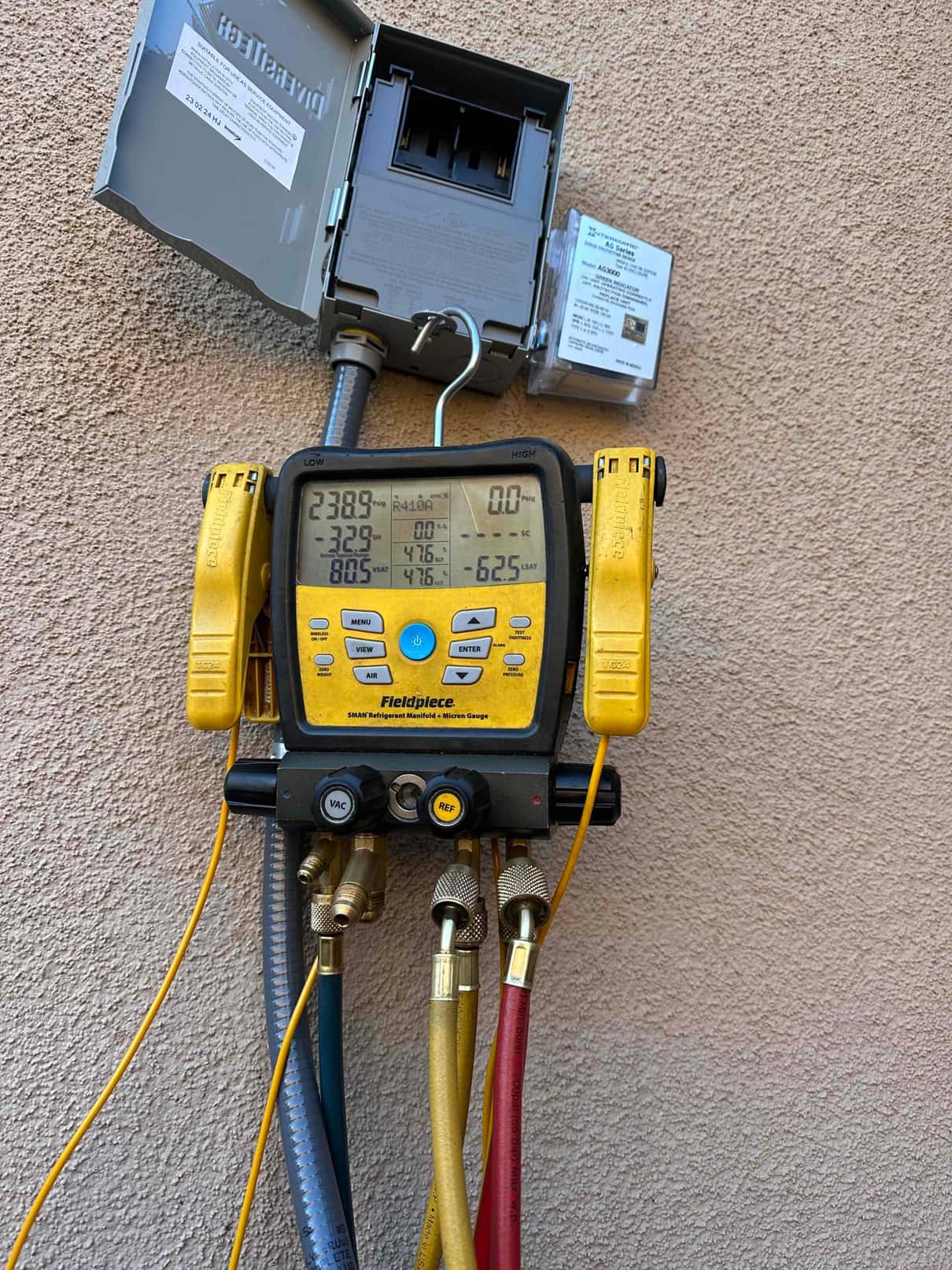 Digital manifold gauges show operating pressures with the system running during commissioning beside the outdoor disconnect box.
