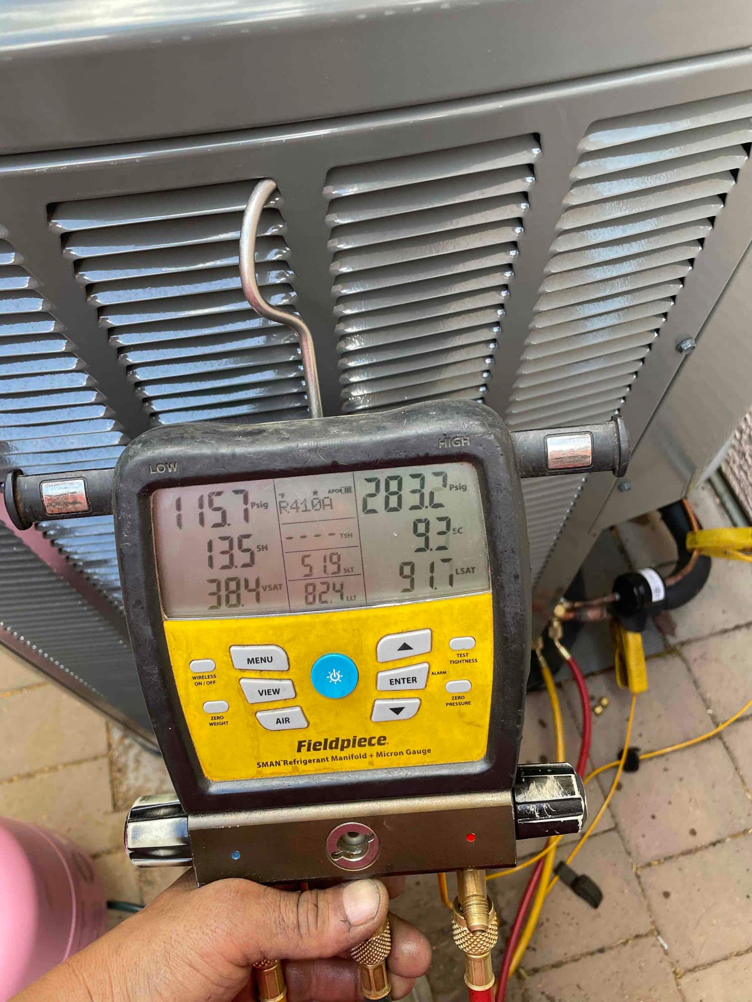 Digital manifold on an outdoor condenser shows operating pressures with superheat and subcooling during system commissioning.