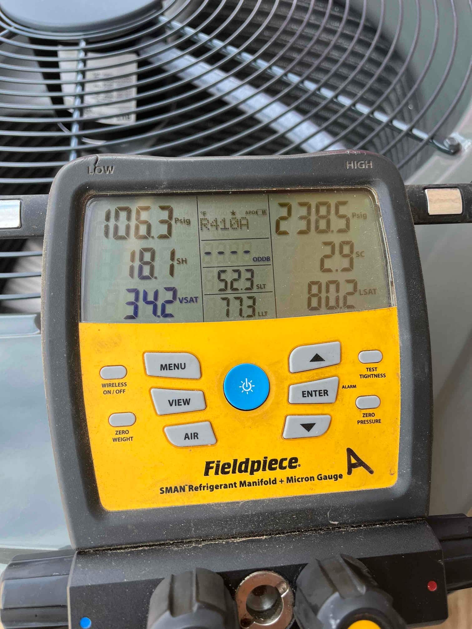 Digital manifold shows operating pressures and temperatures while the outdoor unit runs during refrigerant commissioning.