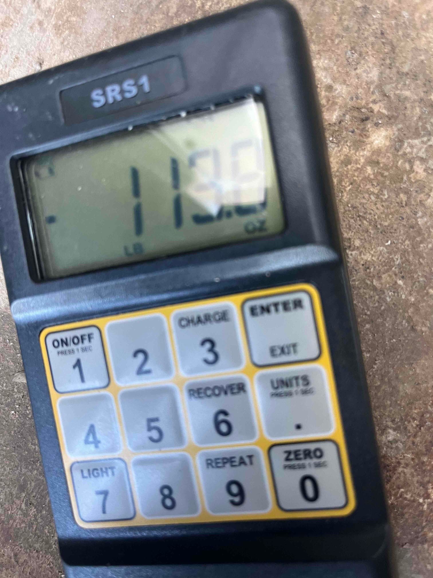 Digital refrigerant scale controller displays 11.30 on the screen with control keypad visible on a jobsite surface.