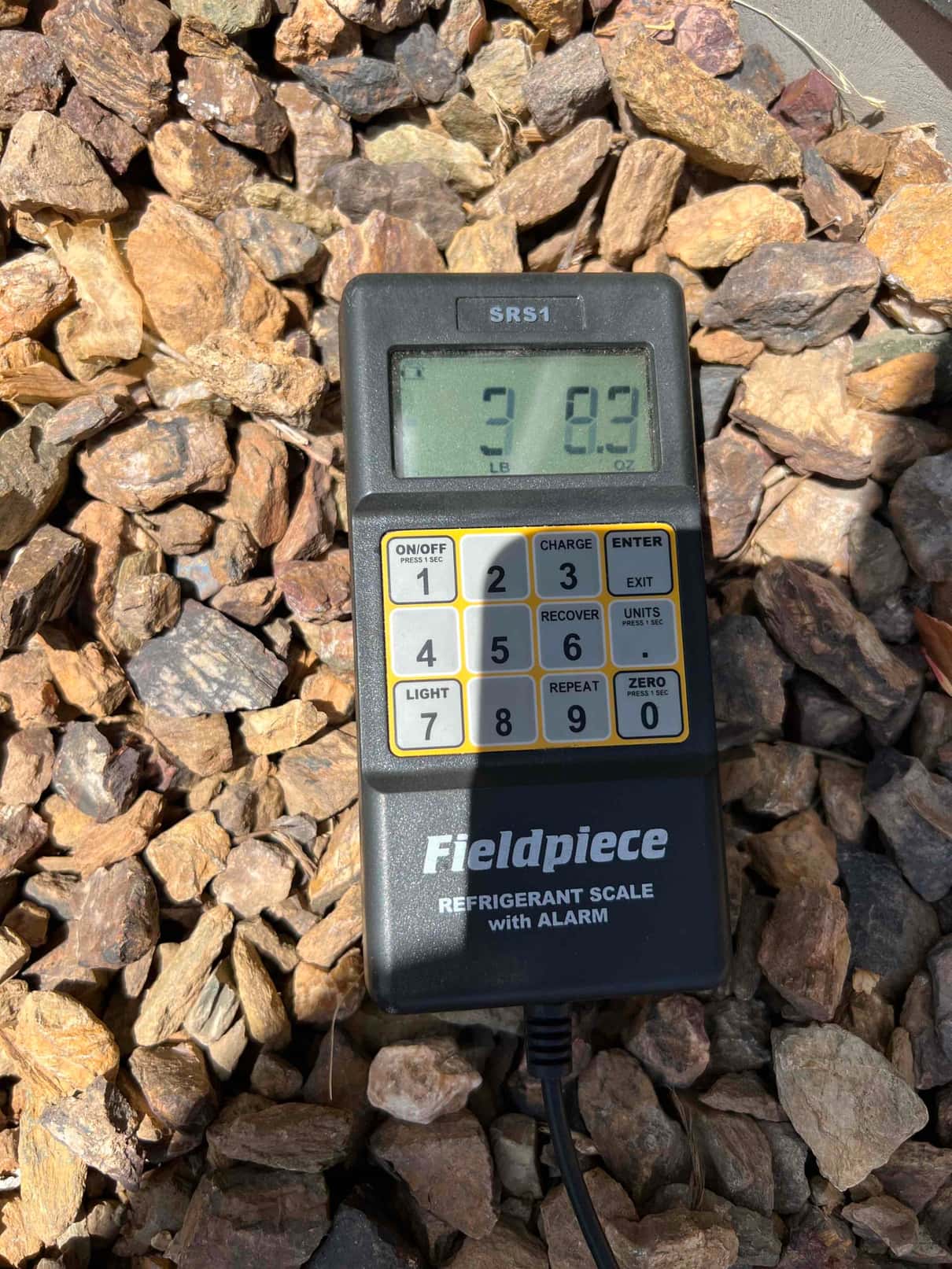 Digital refrigerant scale controller displays 3 pounds 8.3 ounces on the screen during charging setup outdoors.