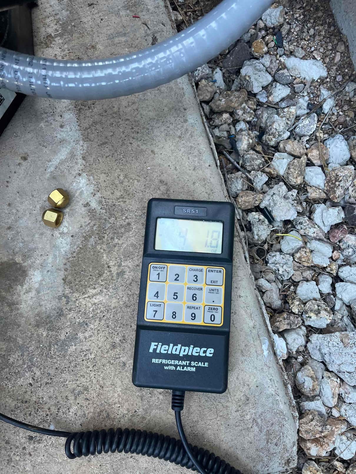 Digital refrigerant scale controller on the jobsite concrete pad, used to meter charge during system commissioning.