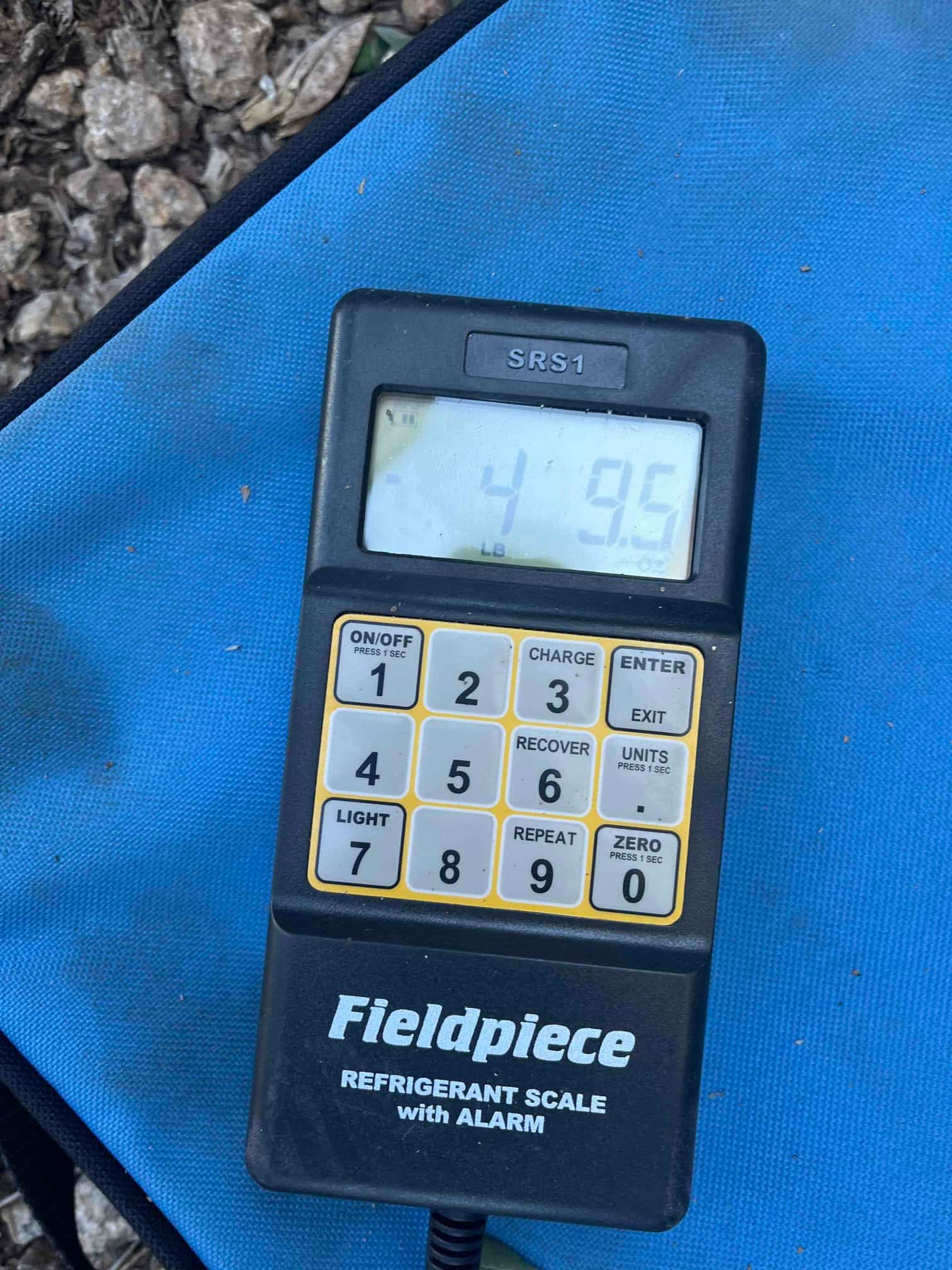 Digital refrigerant scale controller on a jobsite mat displaying 49.5 pounds during system charging process.