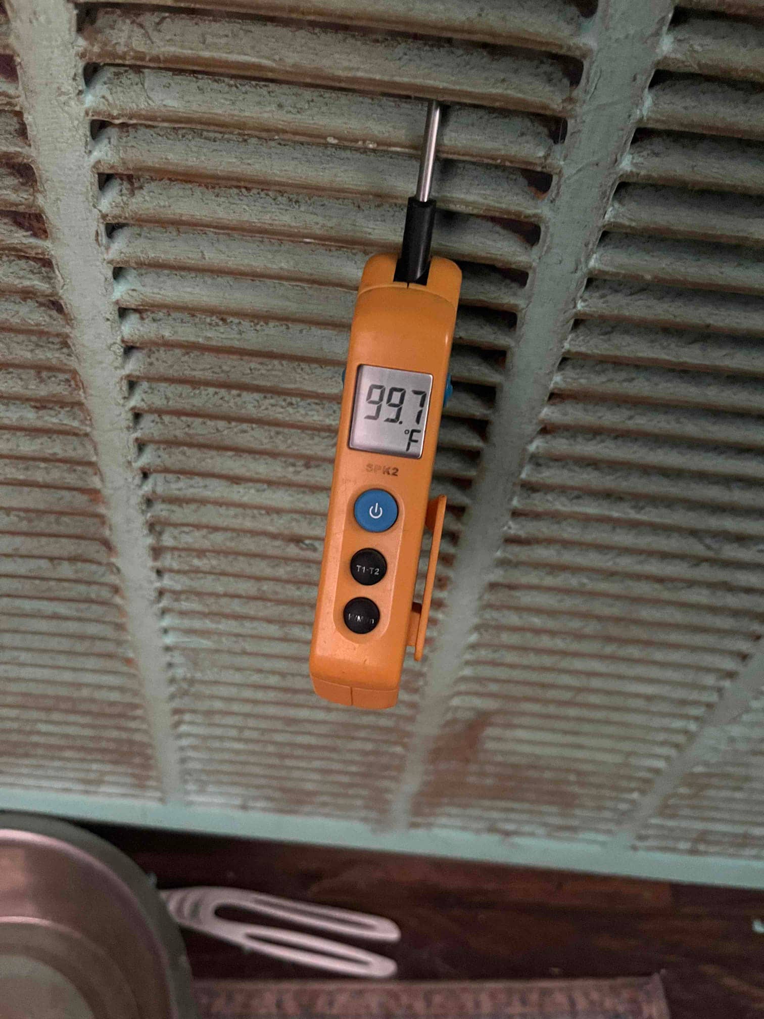 Digital thermometer clipped at a grille shows 99.7 °F air temperature on the display.