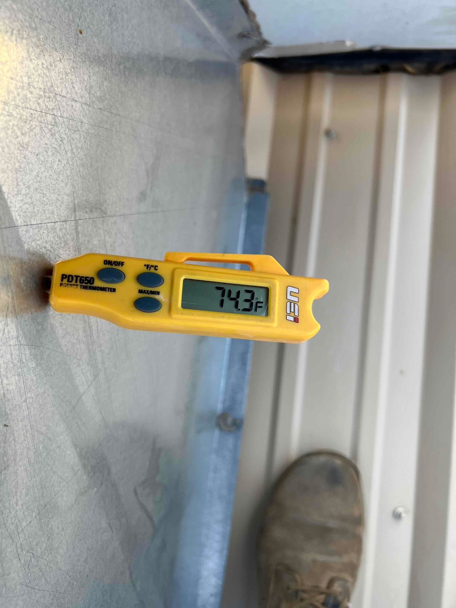 Digital thermometer displays 74.3 °F while measuring the surface temperature of a metal HVAC panel.