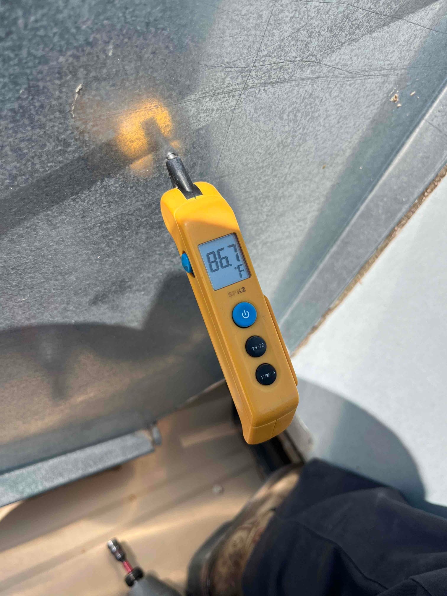 Digital thermometer measures 86.7 °F on a metal surface, probe inserted at the contact point for temperature reading.
