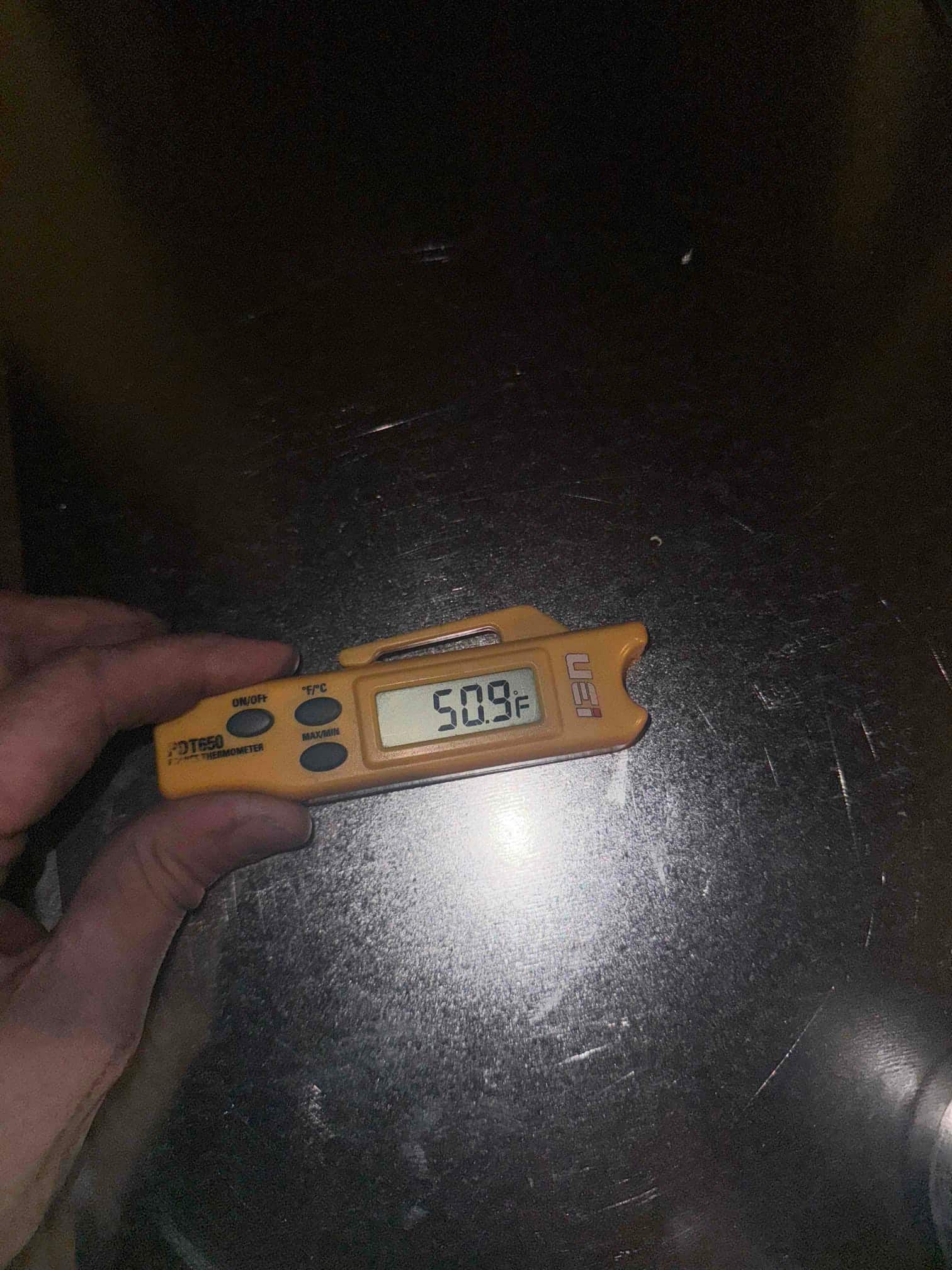 Digital thermometer placed on metal ductwork shows 50.9°F, documenting supply air temperature after the evaporator during cooling operation.