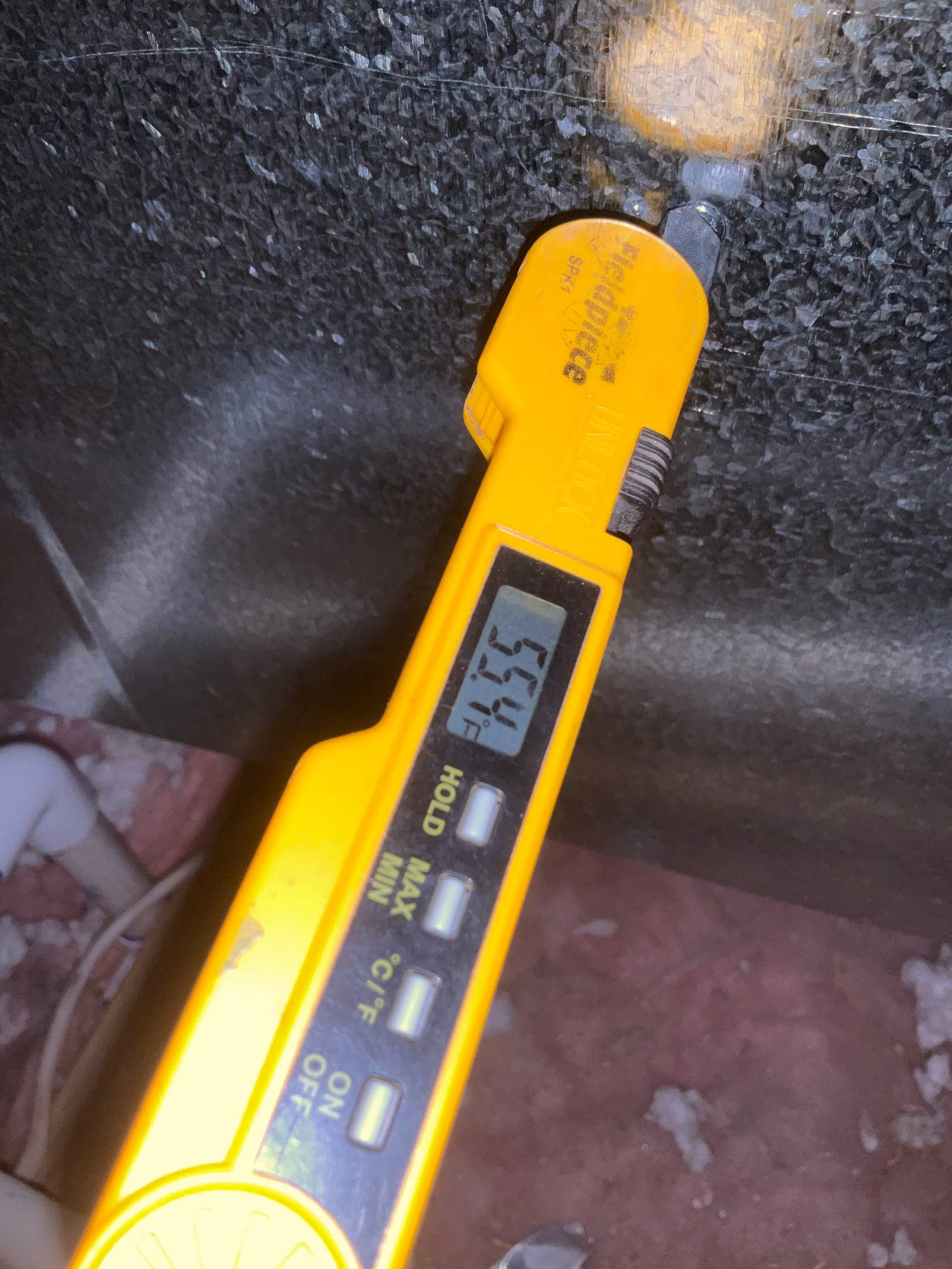 Digital thermometer probe measures supply air temperature at 55.4°F on the duct surface during system checkout.
