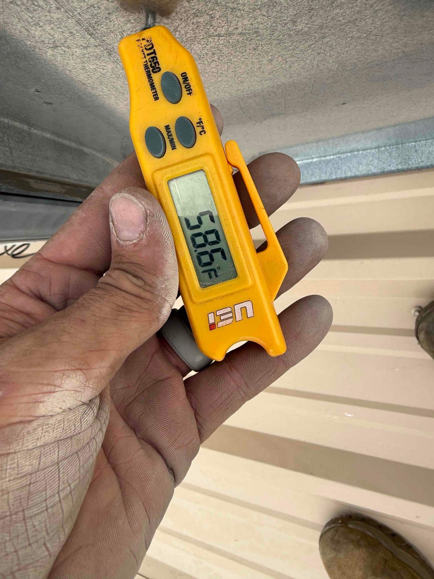 Digital thermometer shows 50.6 °F on the probe while measuring temperature at the HVAC repair site.