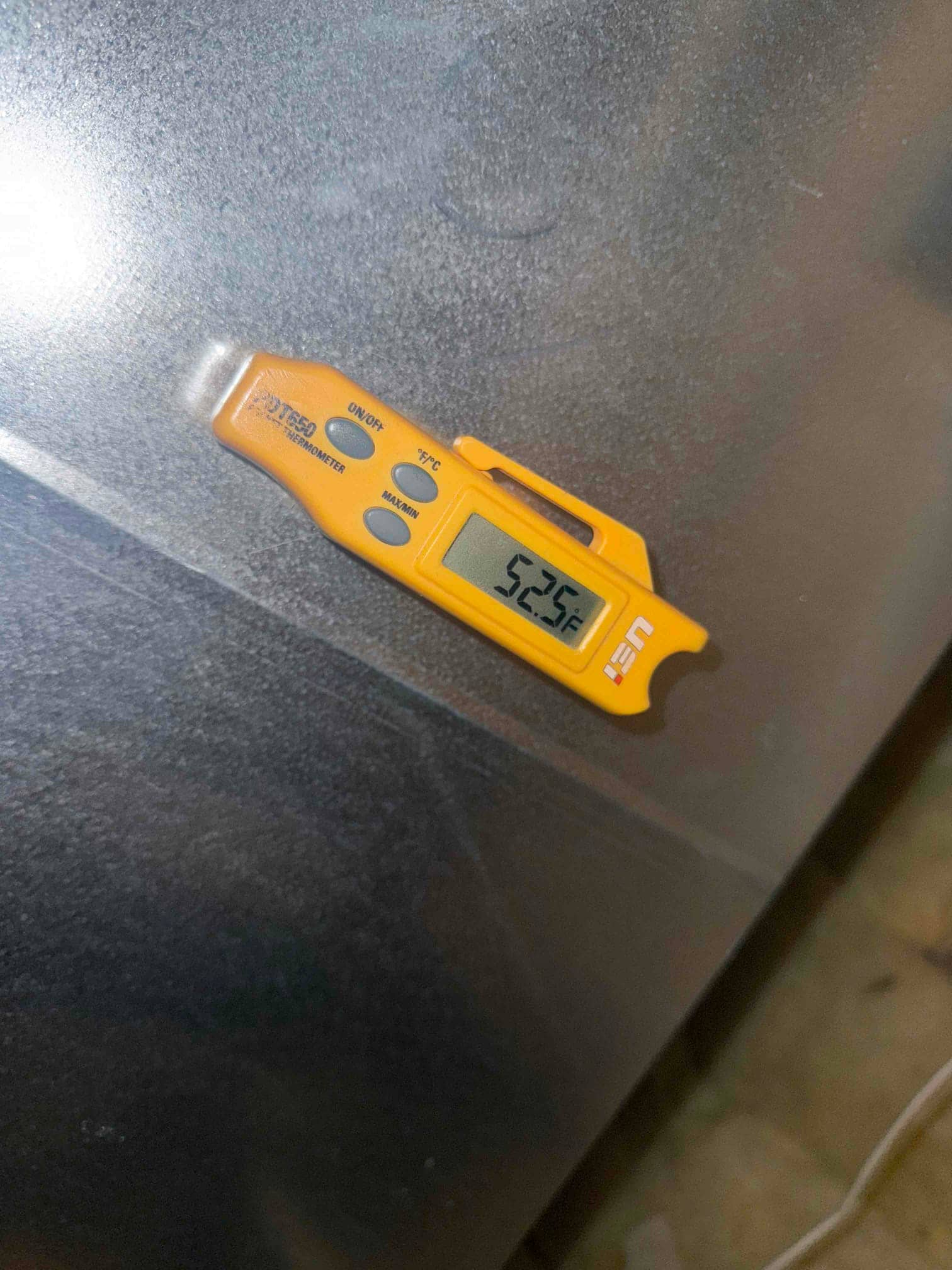 Digital thermometer shows 52.5°F while measuring supply air temperature on the metal supply plenum surface.