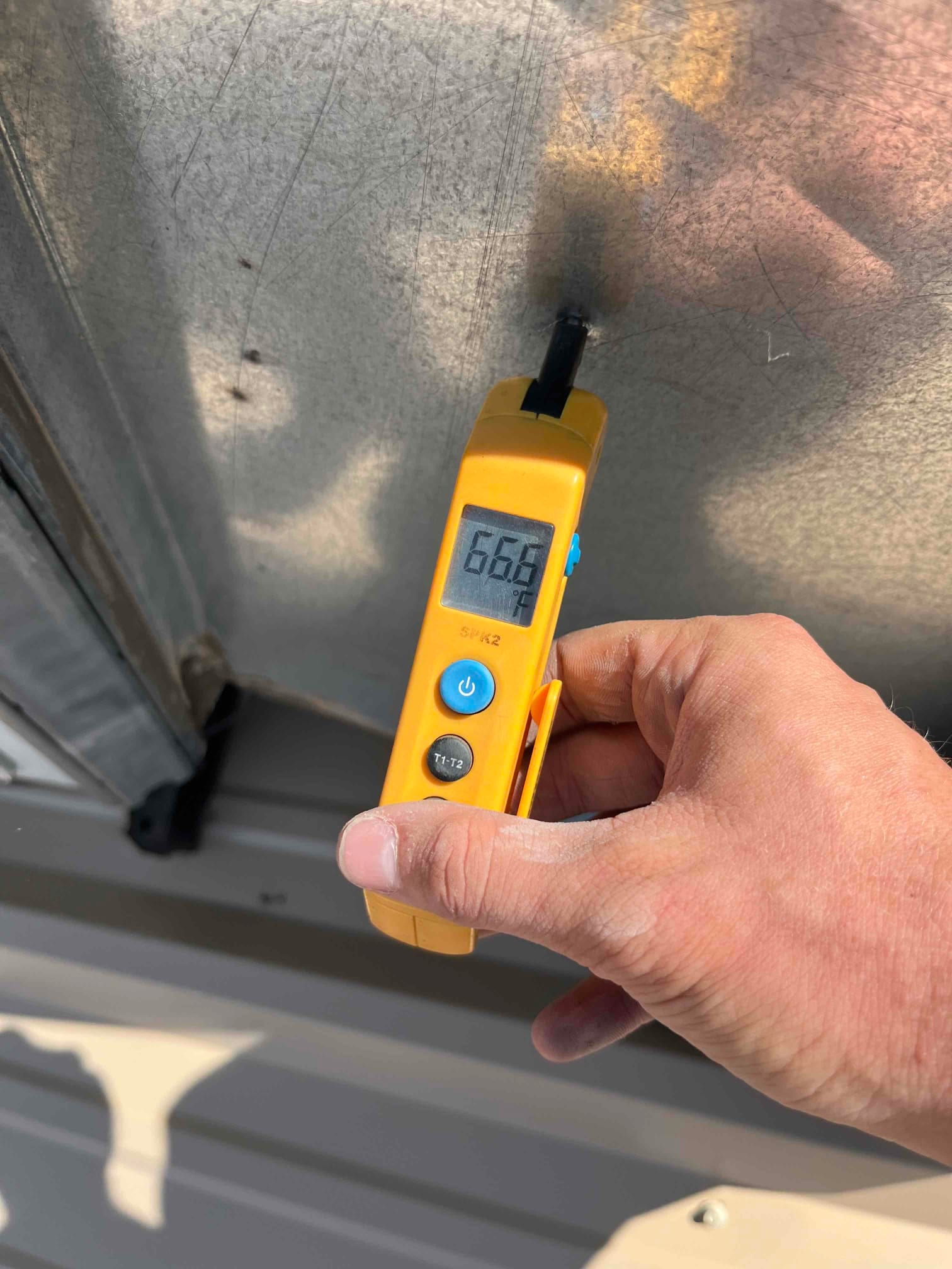 Digital thermometer shows 66.6 °F surface temperature on metal HVAC equipment panel during air conditioning repair.