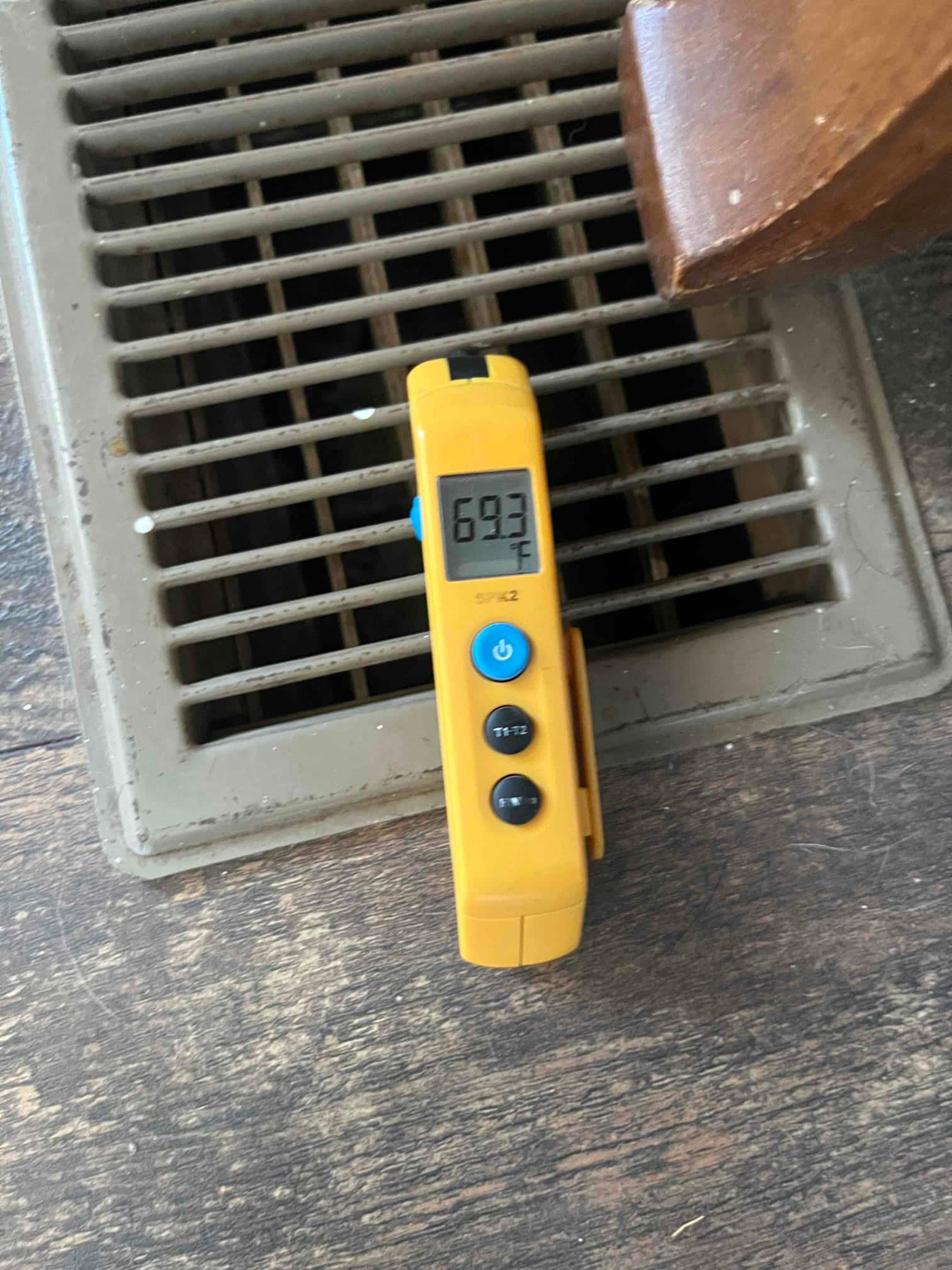 Digital thermometer shows 69.3 °F at a supply floor register during system diagnostic.