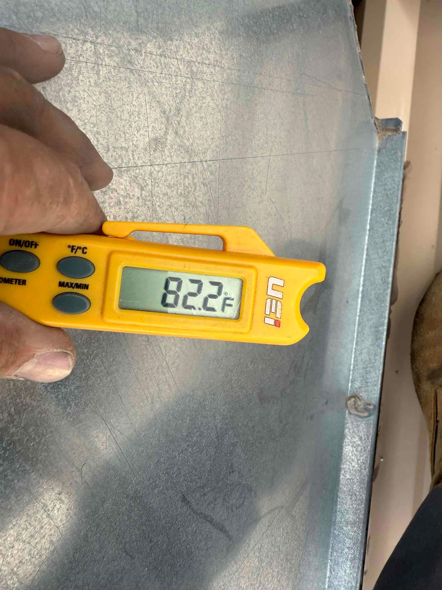 Digital thermometer shows 82.2 °F while measuring temperature on a sheet metal surface at the repair site.