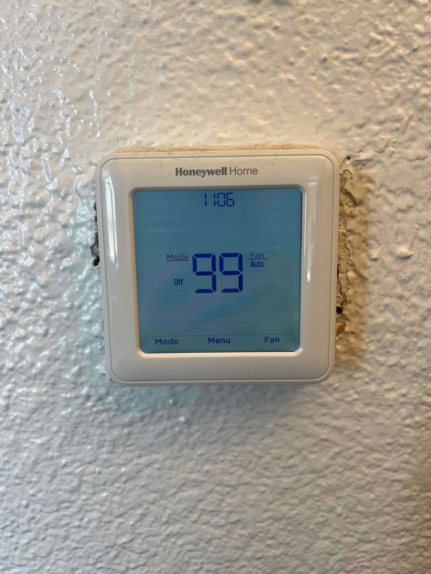 Digital thermostat on wall displays 99 degrees with system mode set to Off and fan set to Auto.
