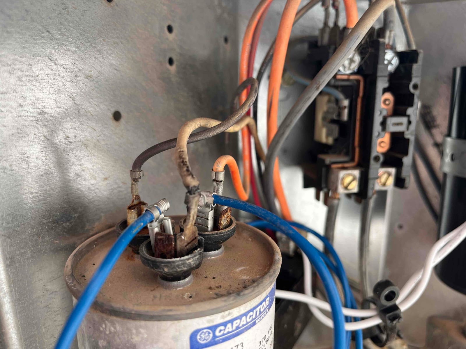 Dual-run capacitor with connected wires and rusted terminals inside the equipment control compartment, contactor visible to the right.