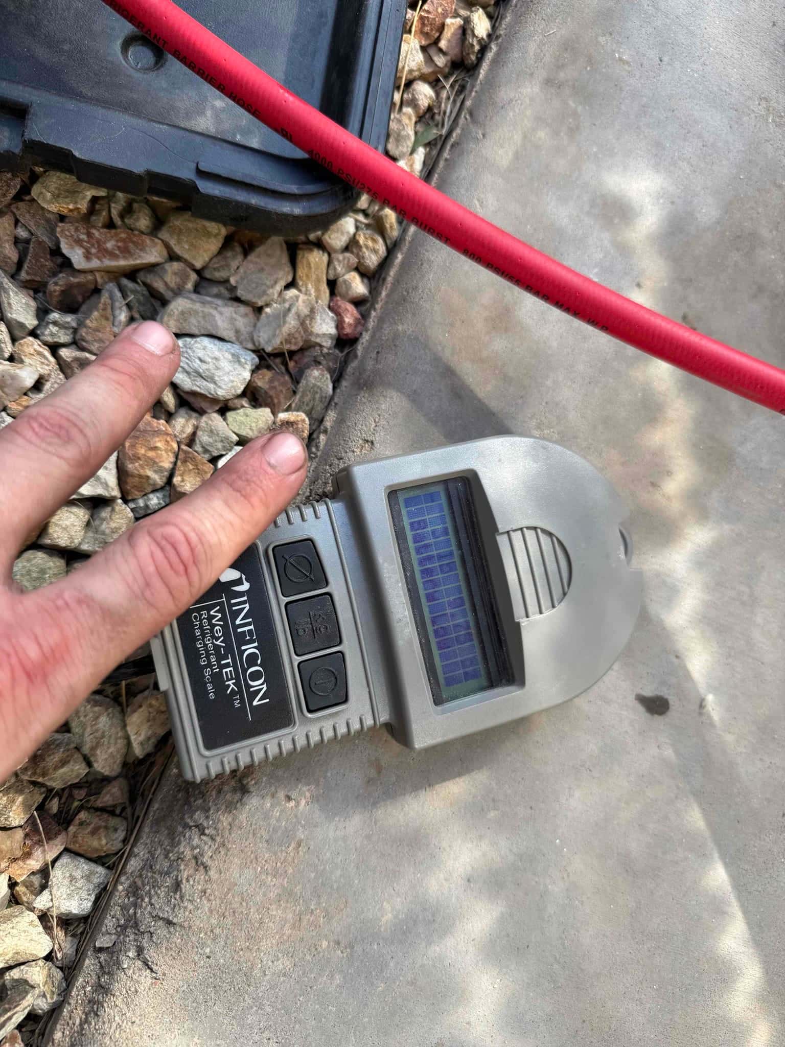 Electronic refrigerant charging scale on the ground with display visible and control buttons, used during system commissioning.