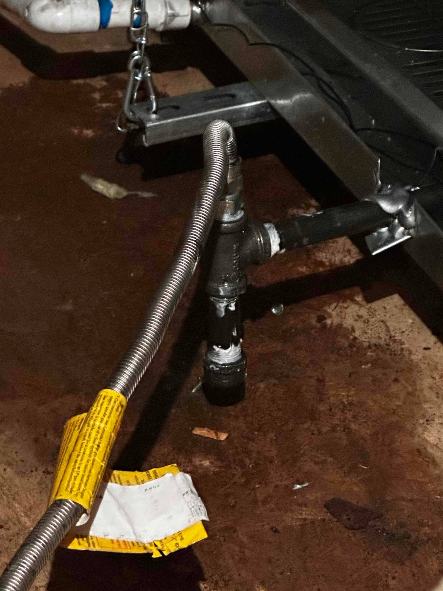 Flexible gas connector with sediment trap and black iron piping installed beside the furnace on a basement floor.