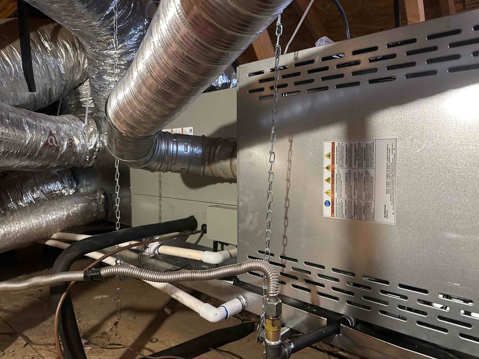 Horizontal air handler hung in attic with insulated flex ducts, drain piping, gas flex connector, and support chains visible.