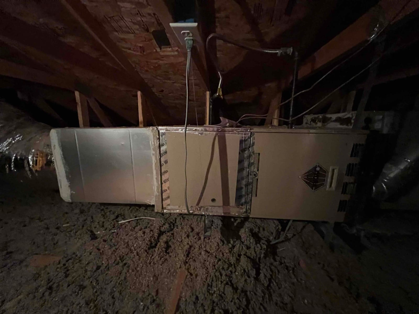 Horizontal HVAC unit in attic with sheet metal plenum and flexible duct connections visible along both ends.