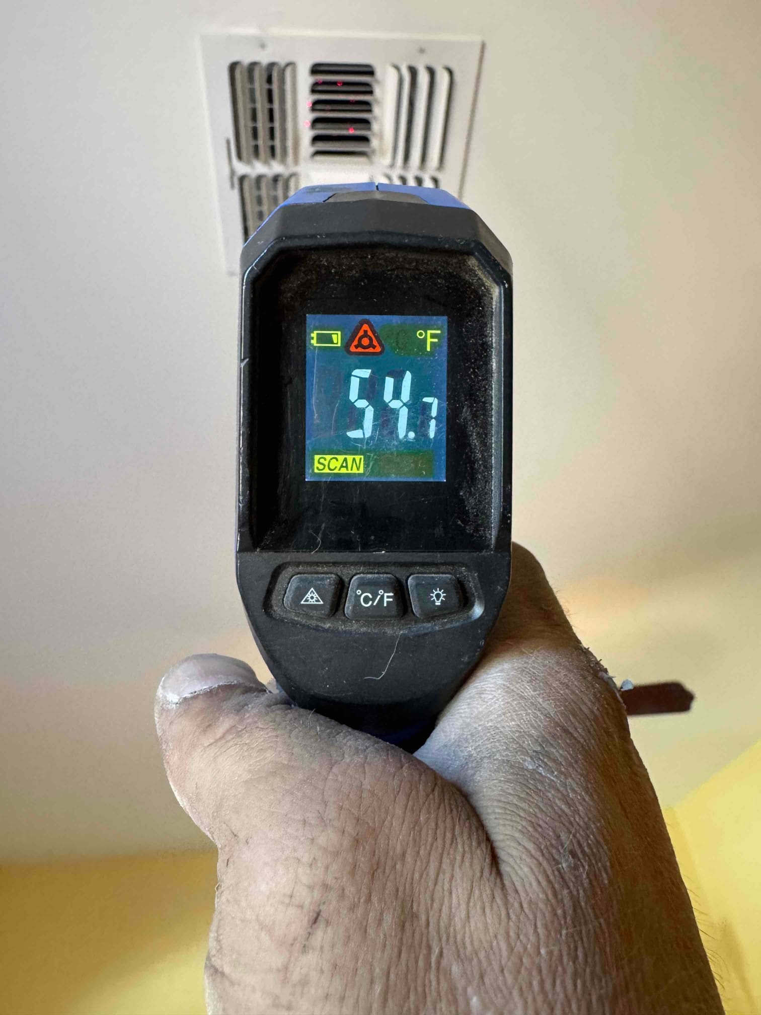 Infrared thermometer measures 54.7°F at a ceiling supply register, documenting cold supply air during system commissioning.