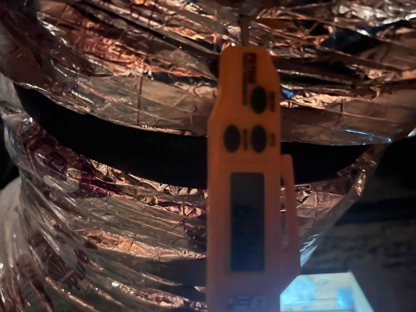 Insulated flexible HVAC duct with reflective foil jacket and a black support strap across it.