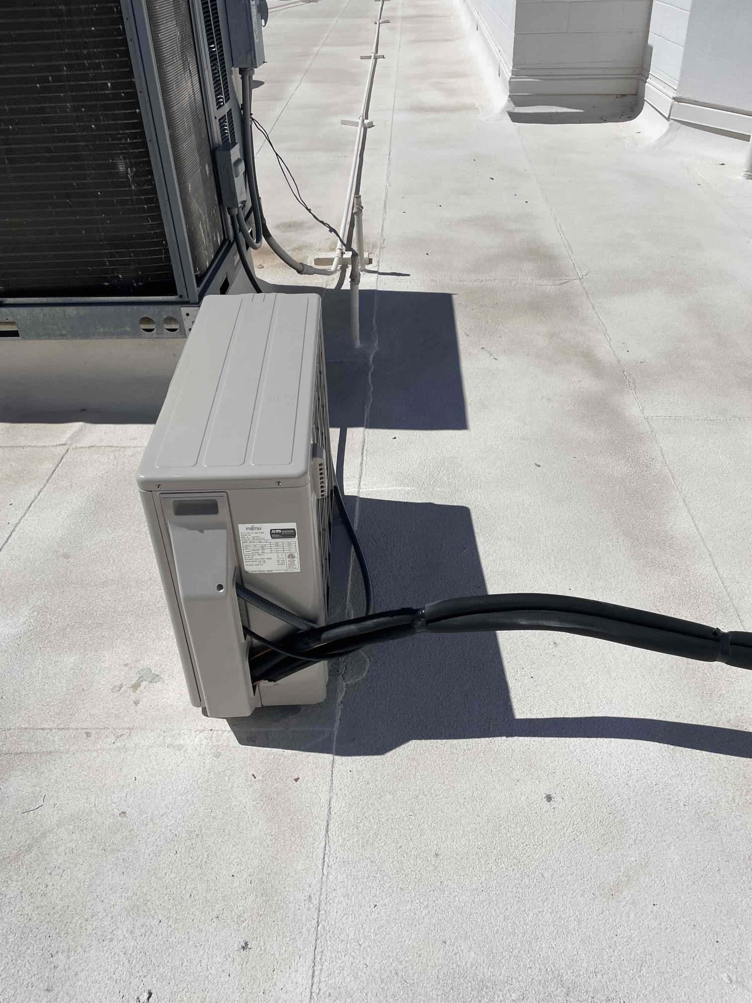 Mini-split condenser set on a roof with insulated refrigerant lines routed to the unit beside existing equipment.