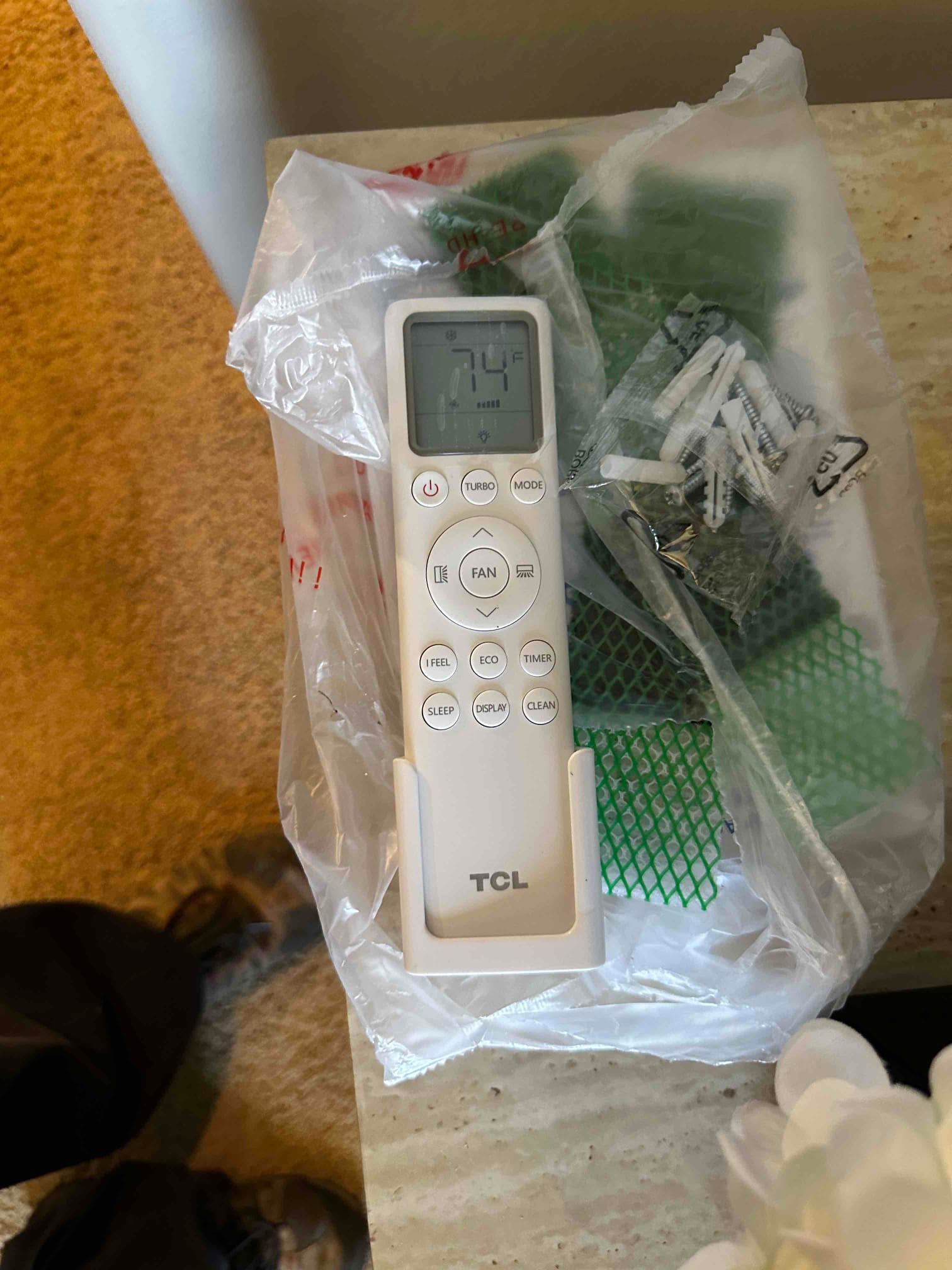 Mini-split remote control on a counter with mounting hardware and holder, display showing 74°F setpoint.