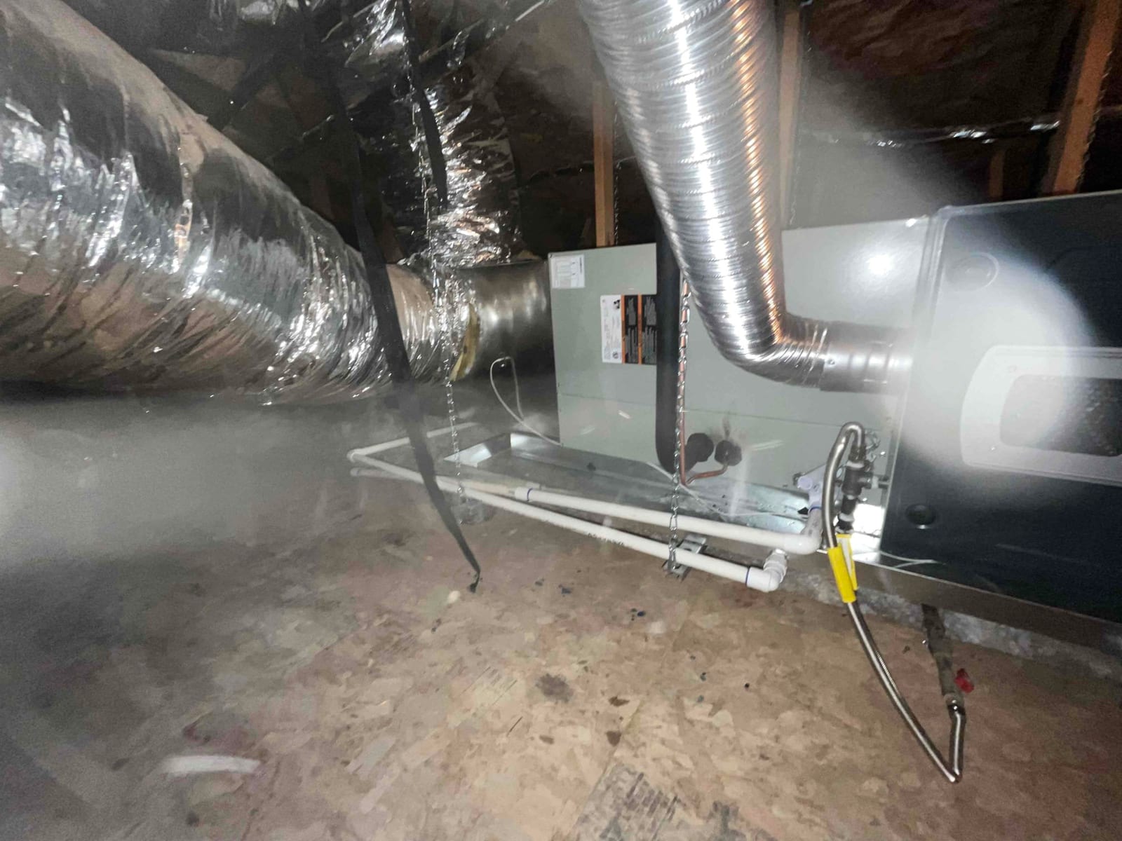 New attic air handler and furnace set with insulated duct connections, condensate drain piping, and gas line hookup on a supported platform.