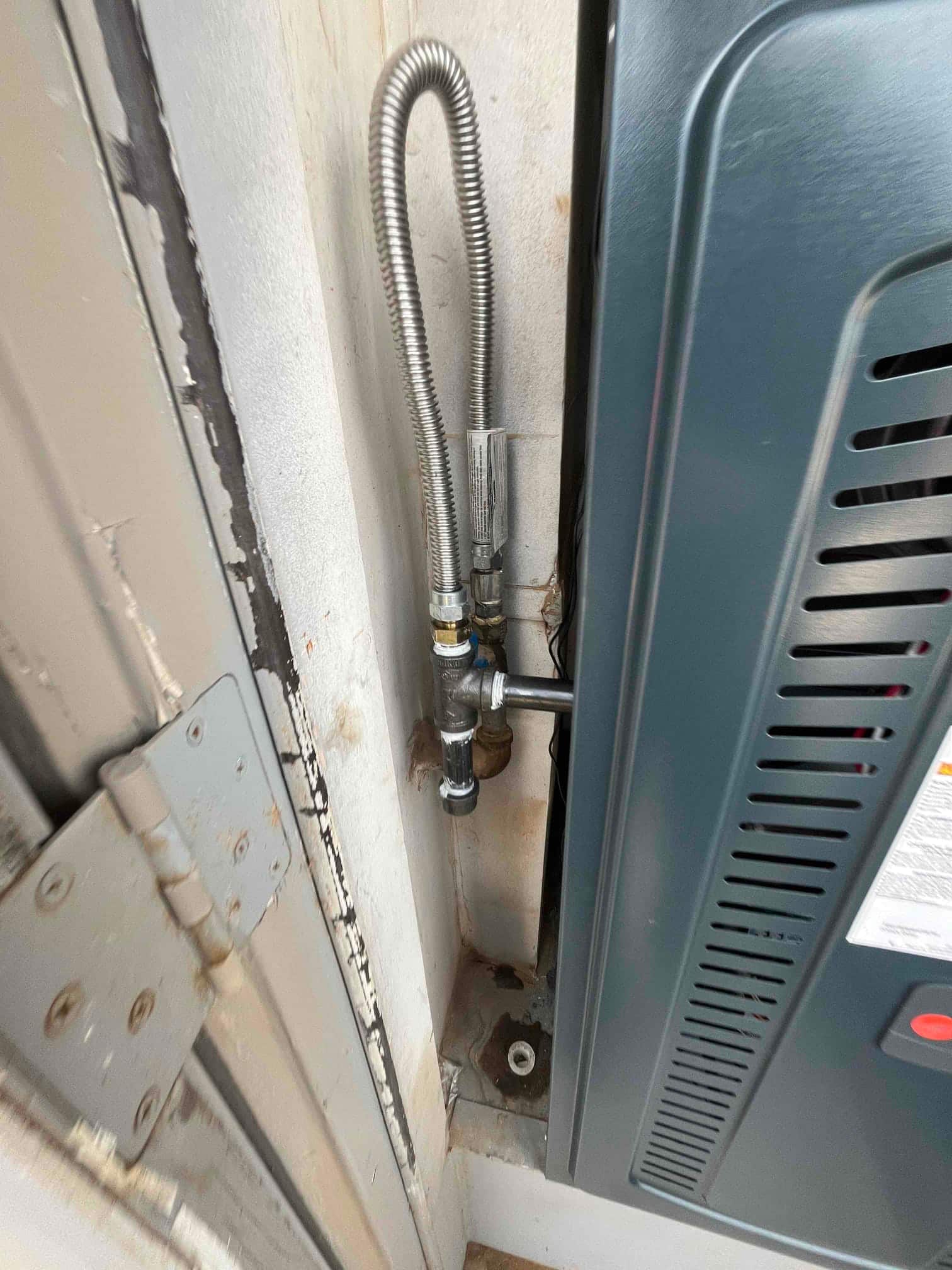 New furnace gas connection with flexible stainless gas line, shutoff valve, and drip leg installed beside the cabinet.