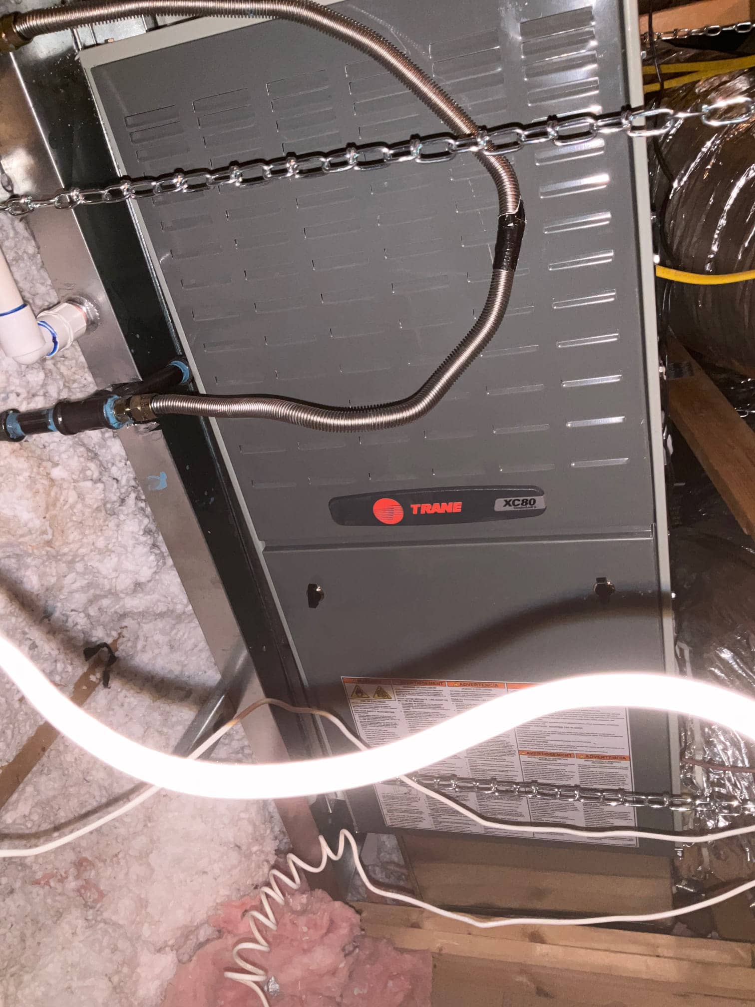 New indoor furnace or air handler installed on a suspended platform with drain plumbing and flexible gas or conduit lines connected.